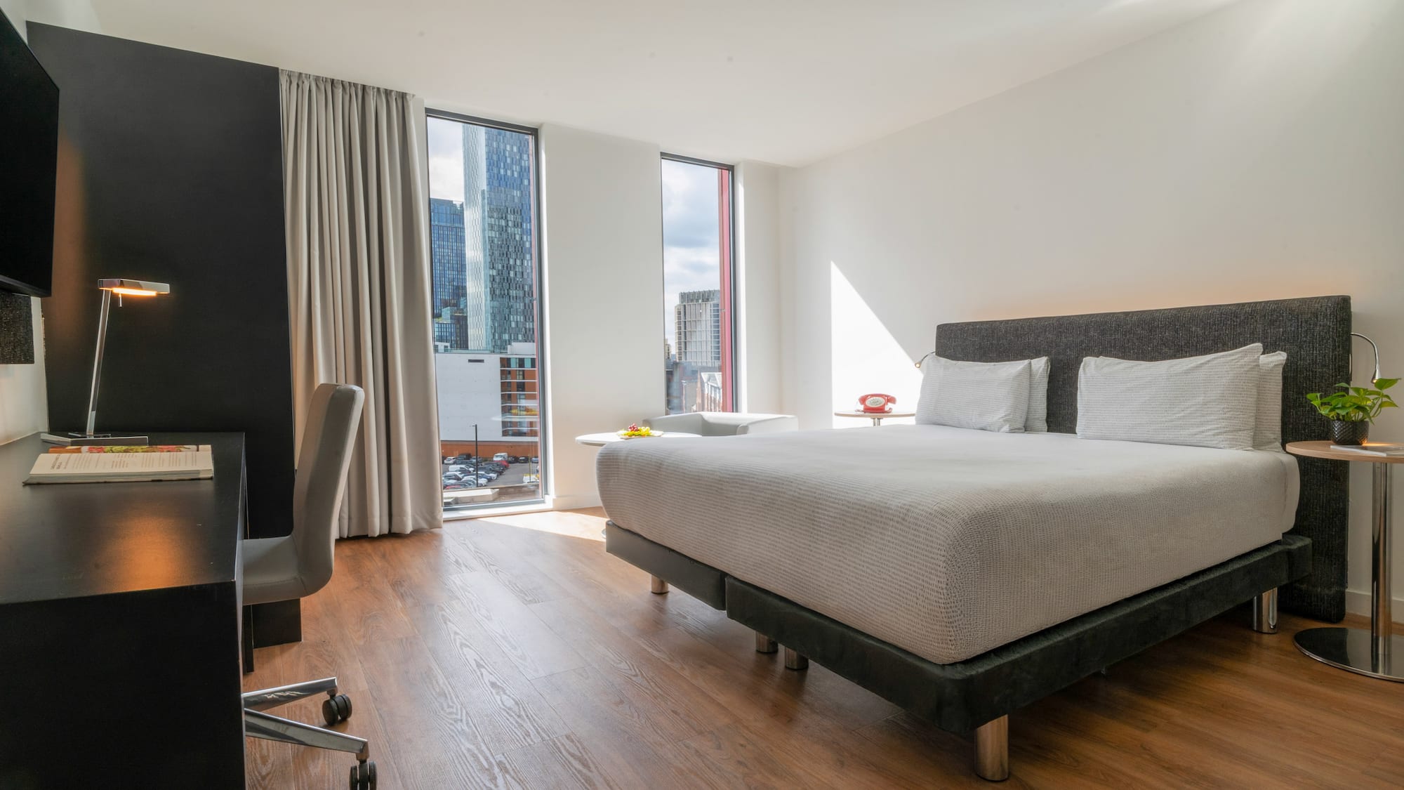 Modern hotel room with city view, bed, and desk.