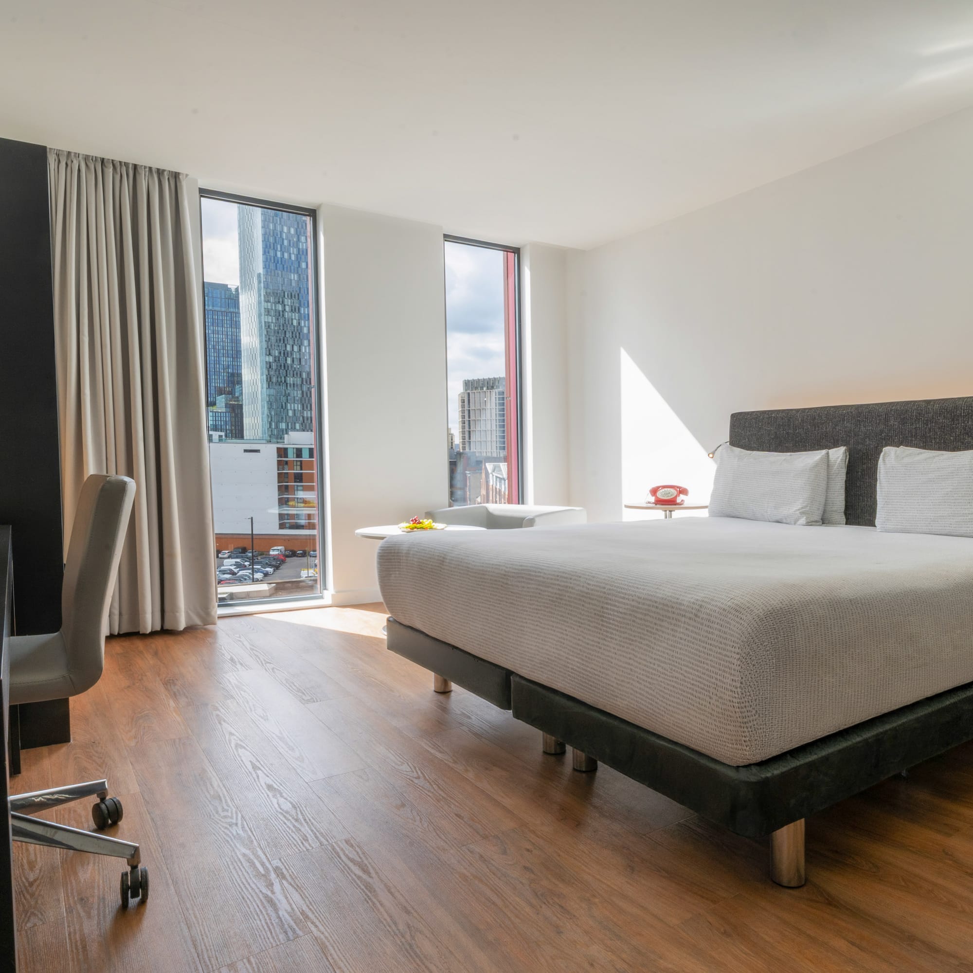 Modern hotel room with city view, bed, and desk.