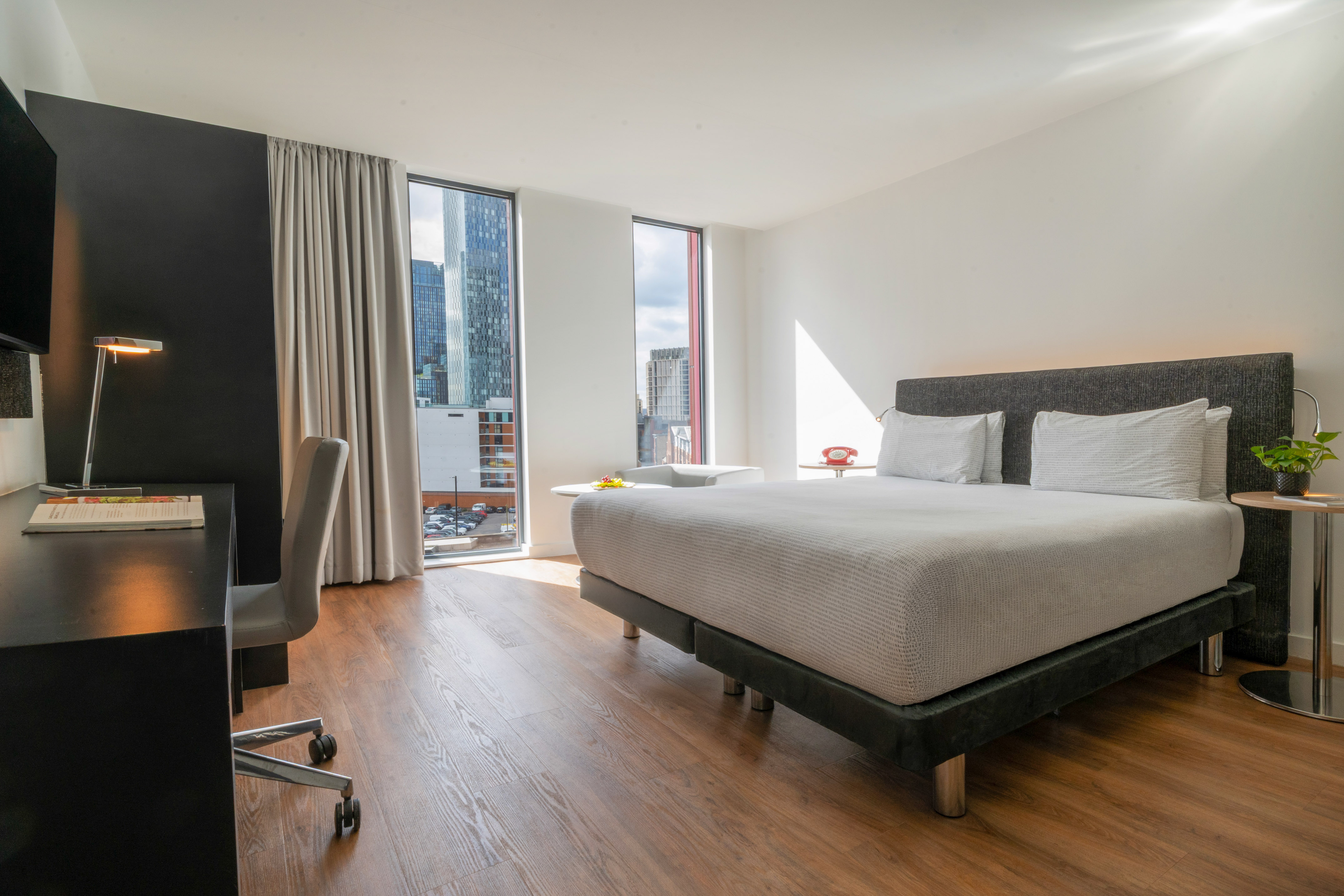 Modern hotel room with city view, bed, and desk.