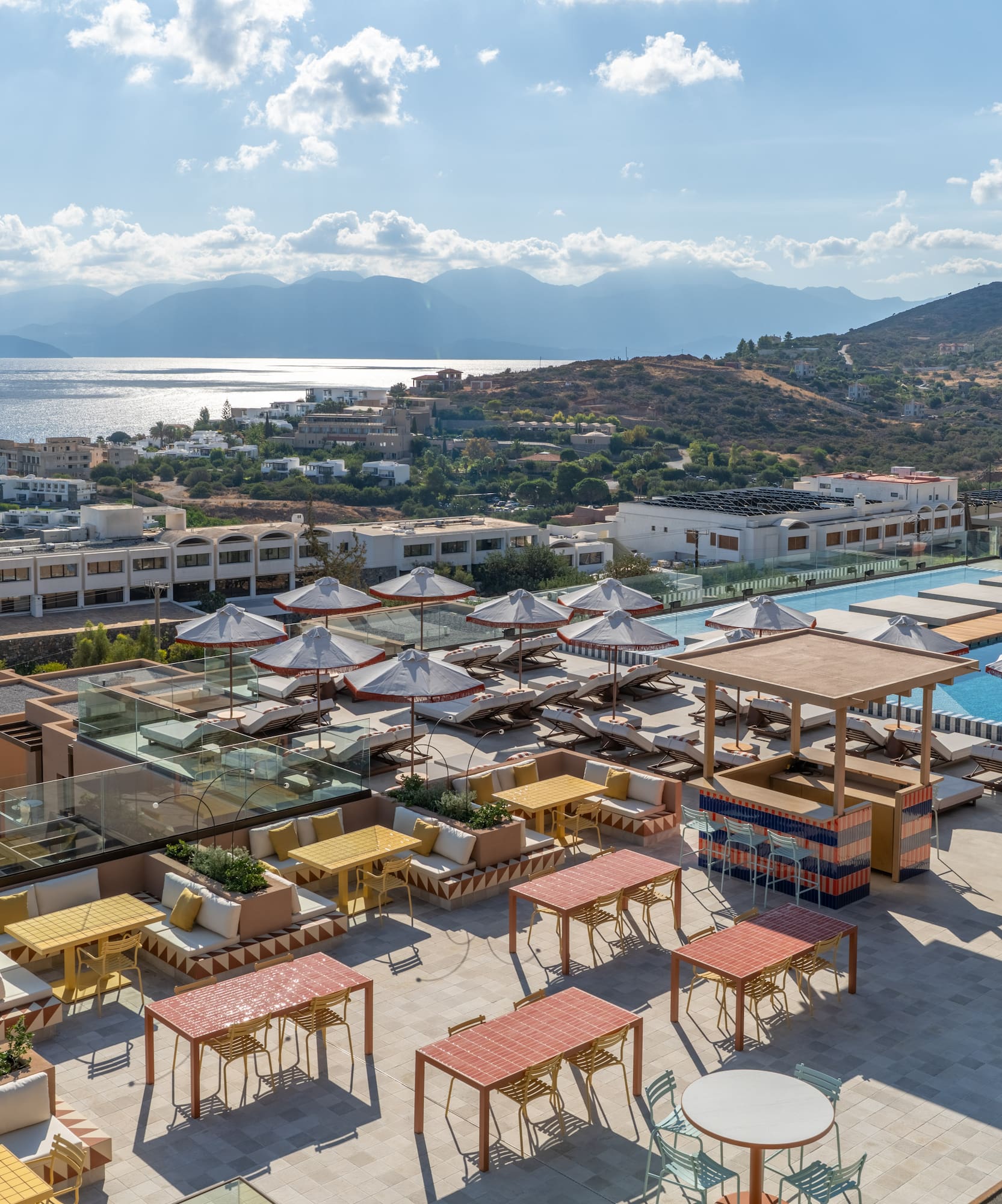 a rooftop patio with tables and umbrellas and a pool in the background