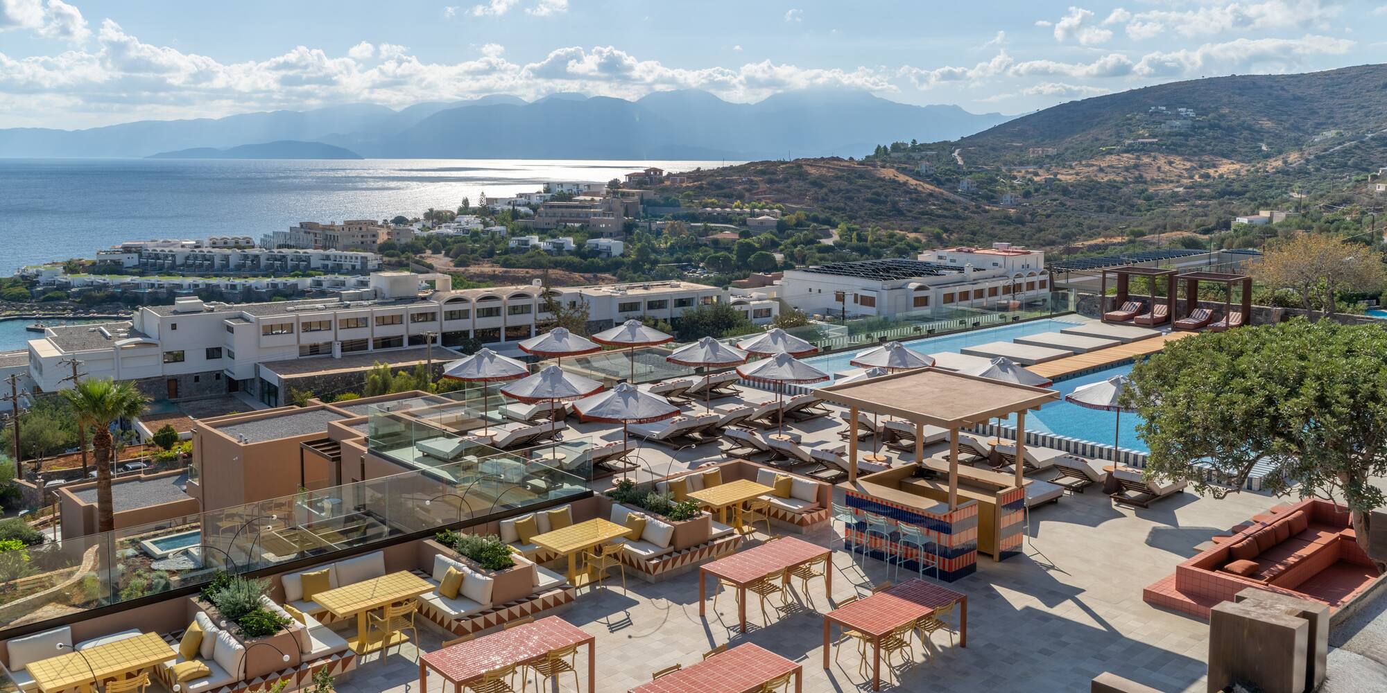a rooftop patio with tables and umbrellas and a pool in the background