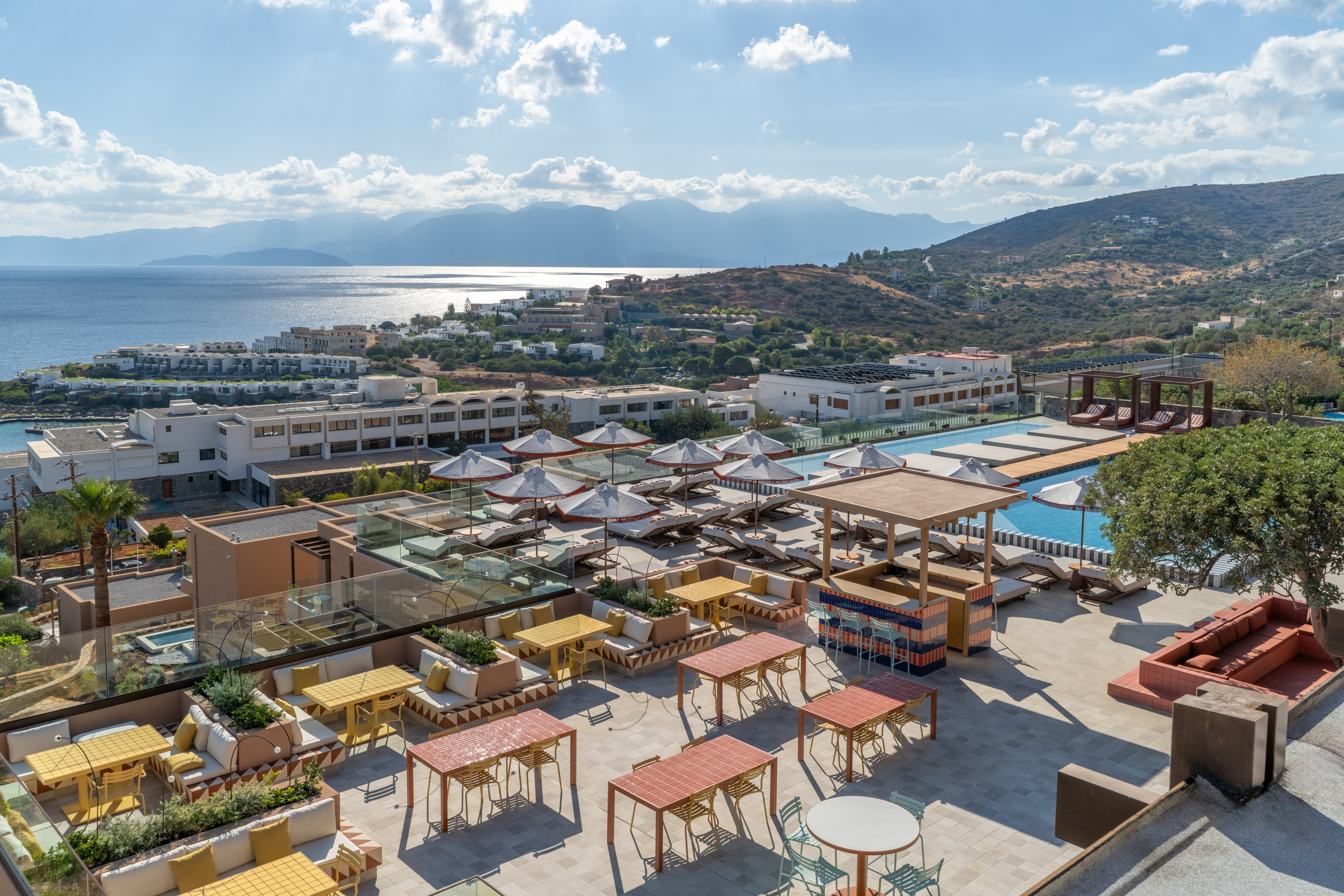 Rooftop resort terrace with colorful dining, pool deck, and coastal sea view.