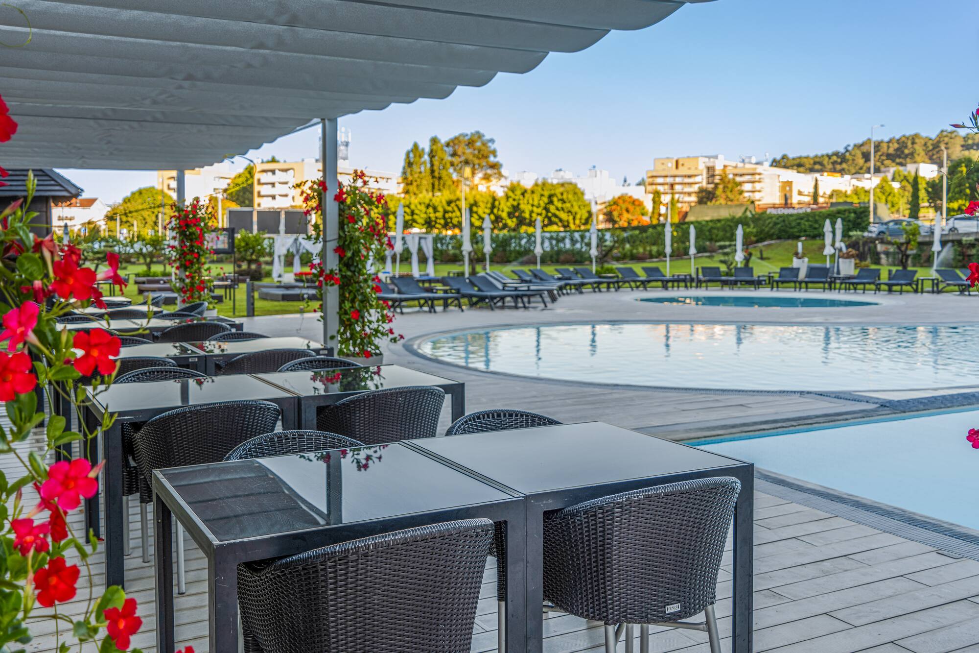 Outdoor dining terrace by a resort pool, with black tables and red flowers.