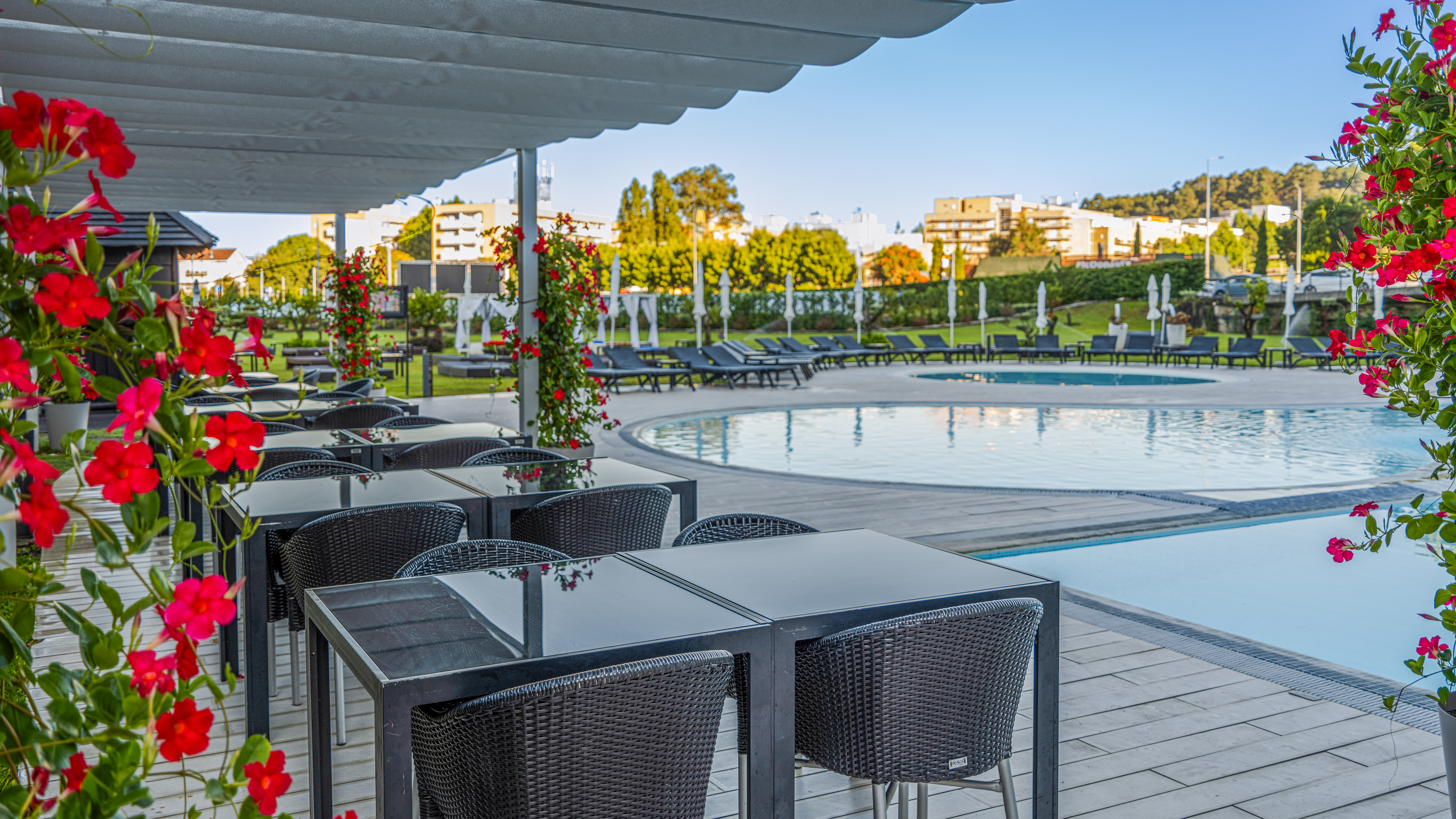 Outdoor dining terrace by a resort pool, with black tables and red flowers.