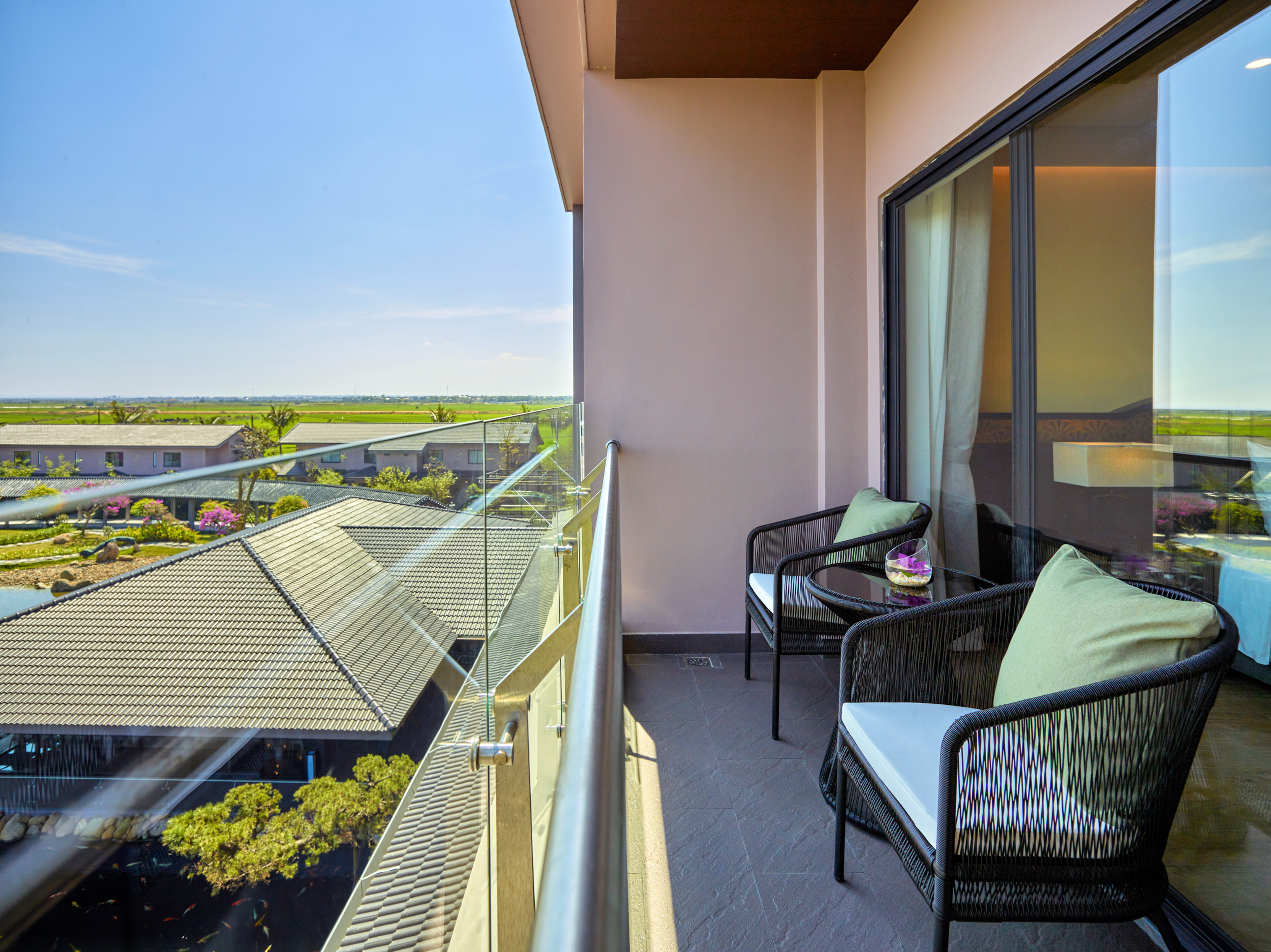 Resort balcony with chairs, glass railing, overlooking paddy fields and koi pond.
