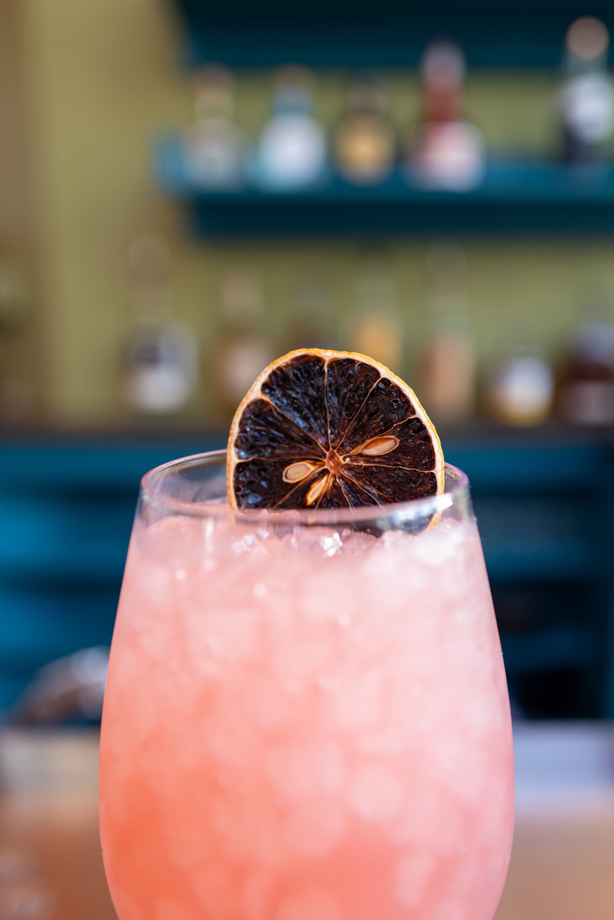Pink cocktail with crushed ice and dried orange slice, blurred bar background. - The Wilson, Cozinha internacional - Meliá Orlando Celebration, Orlando