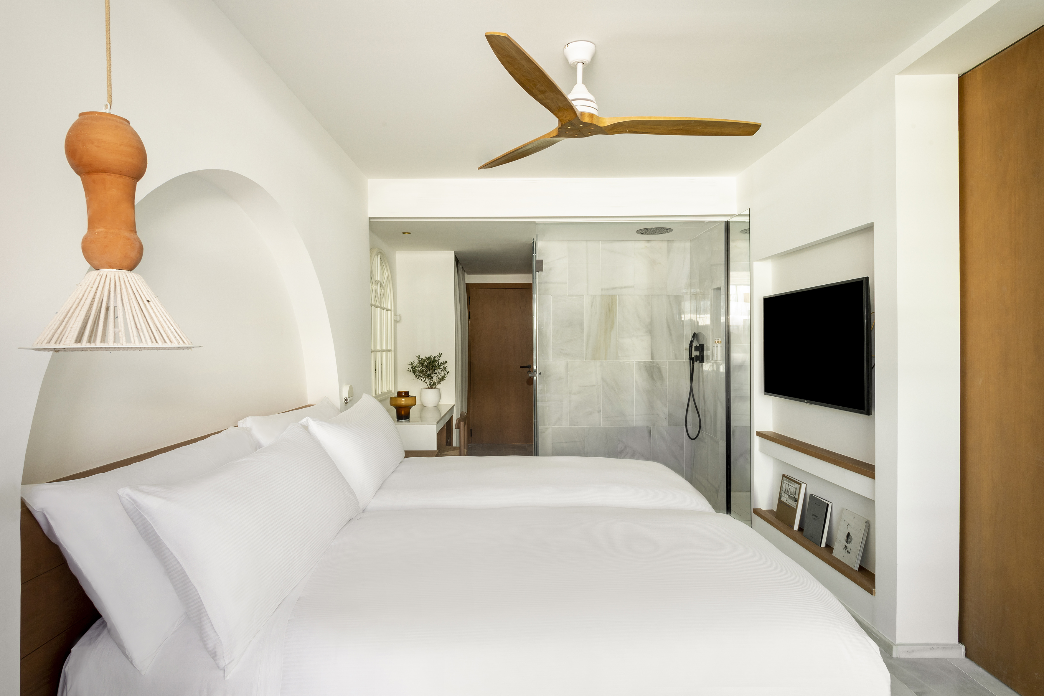 Modern hotel room with twin beds, wood fan, and glass shower.