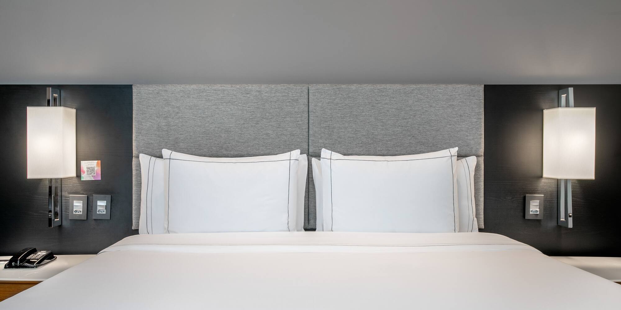 a bed with white sheets and a grey headboard