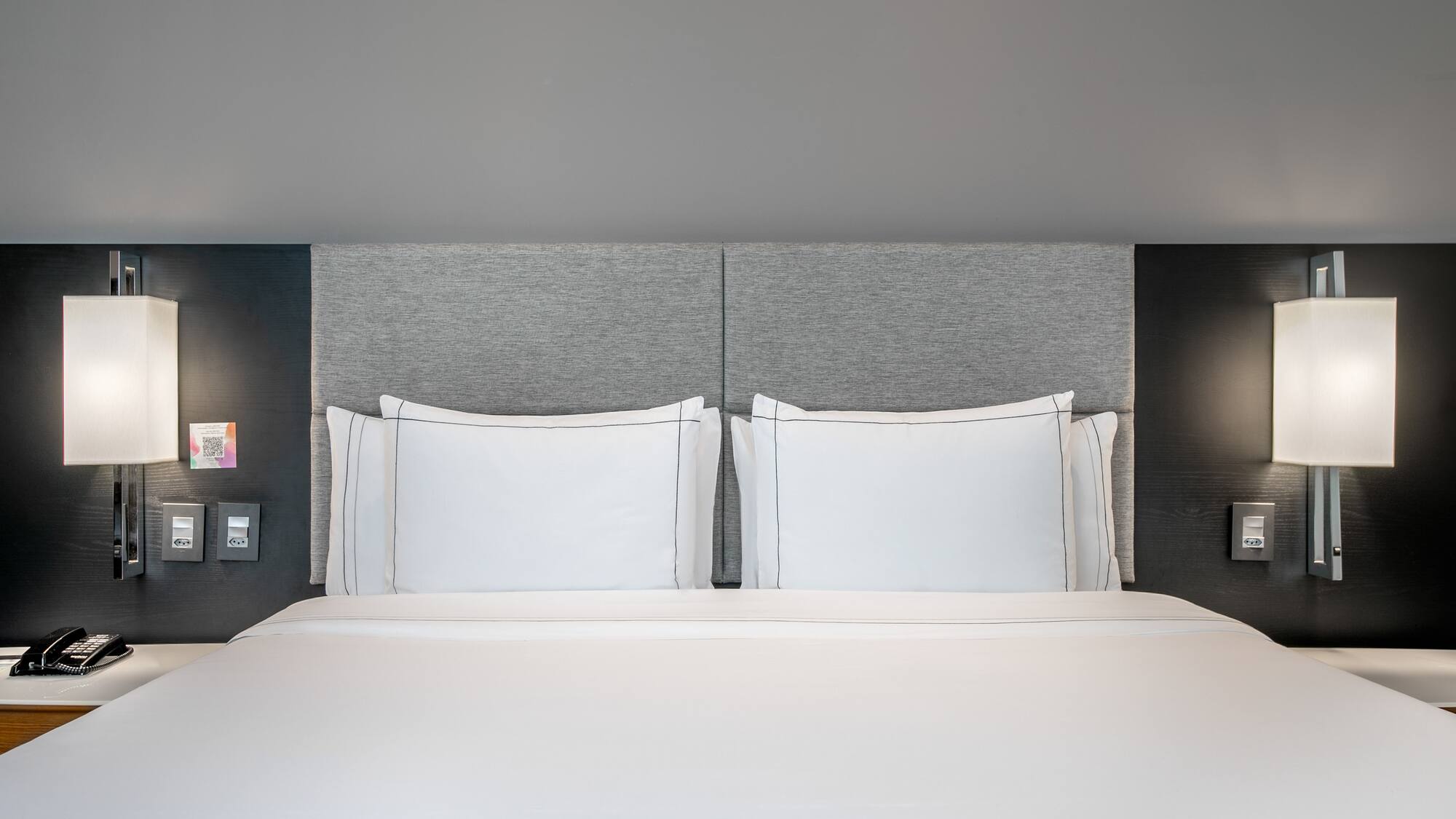 a bed with white sheets and a grey headboard