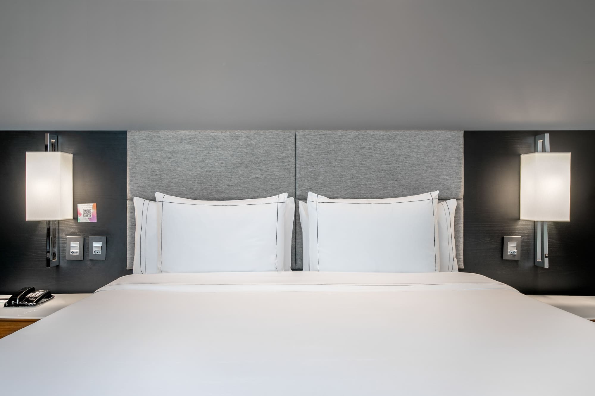 a bed with white sheets and a grey headboard