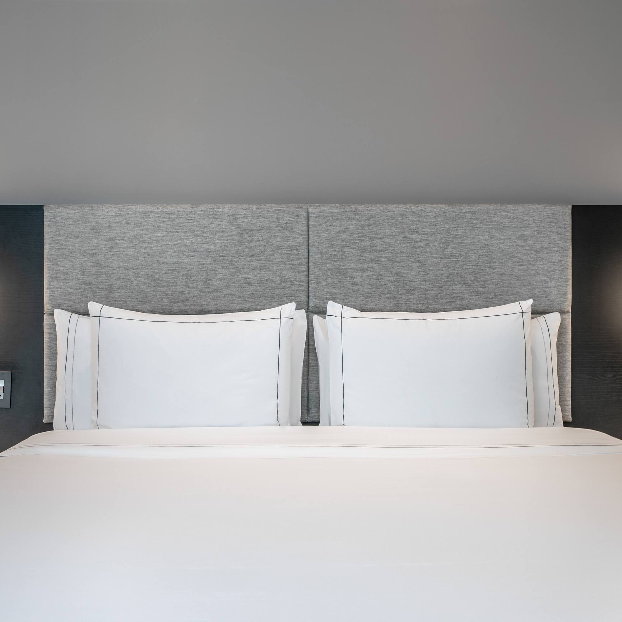 a bed with white sheets and a grey headboard