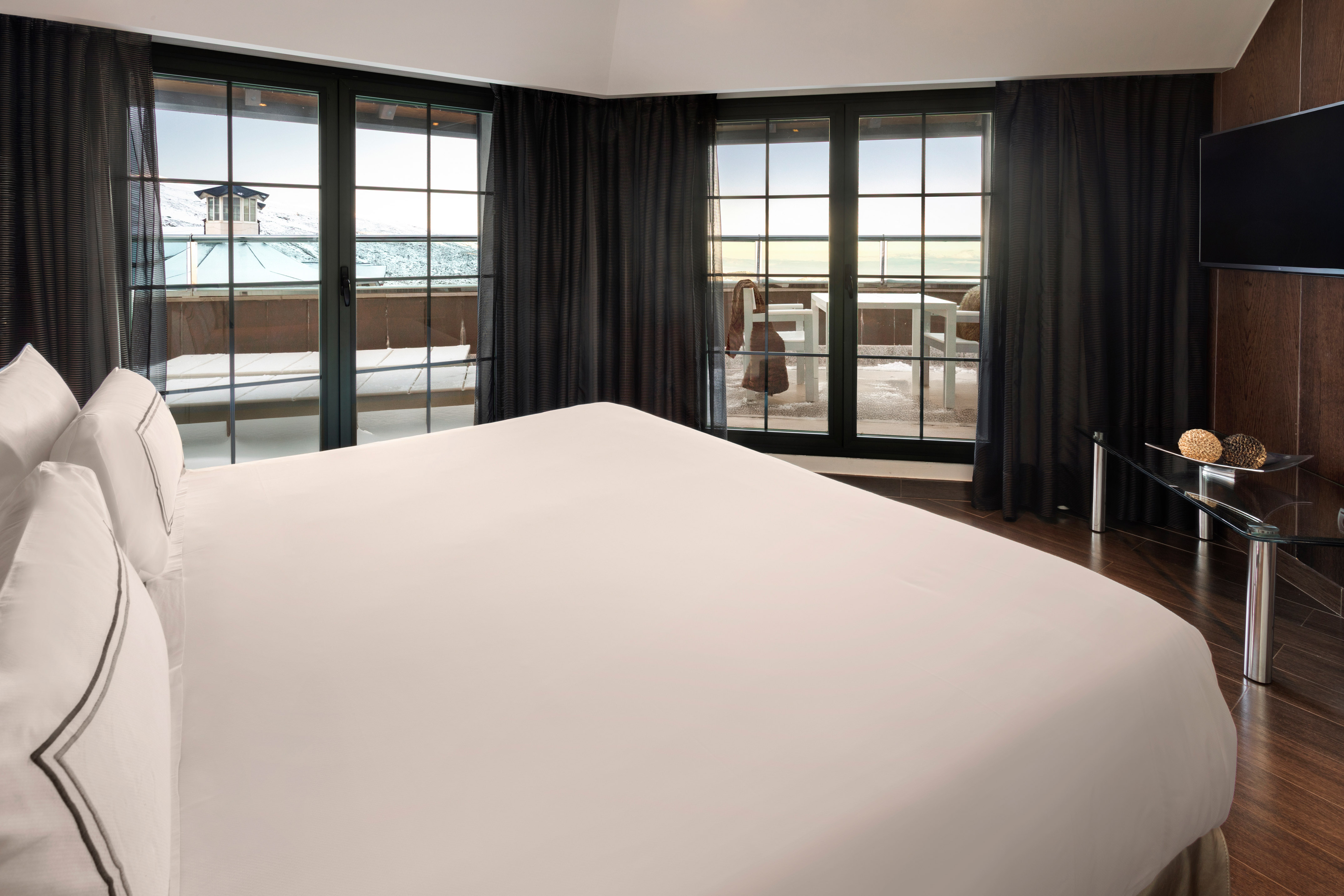 Elegant hotel room with bed, balcony overlooking snowy mountain resort.