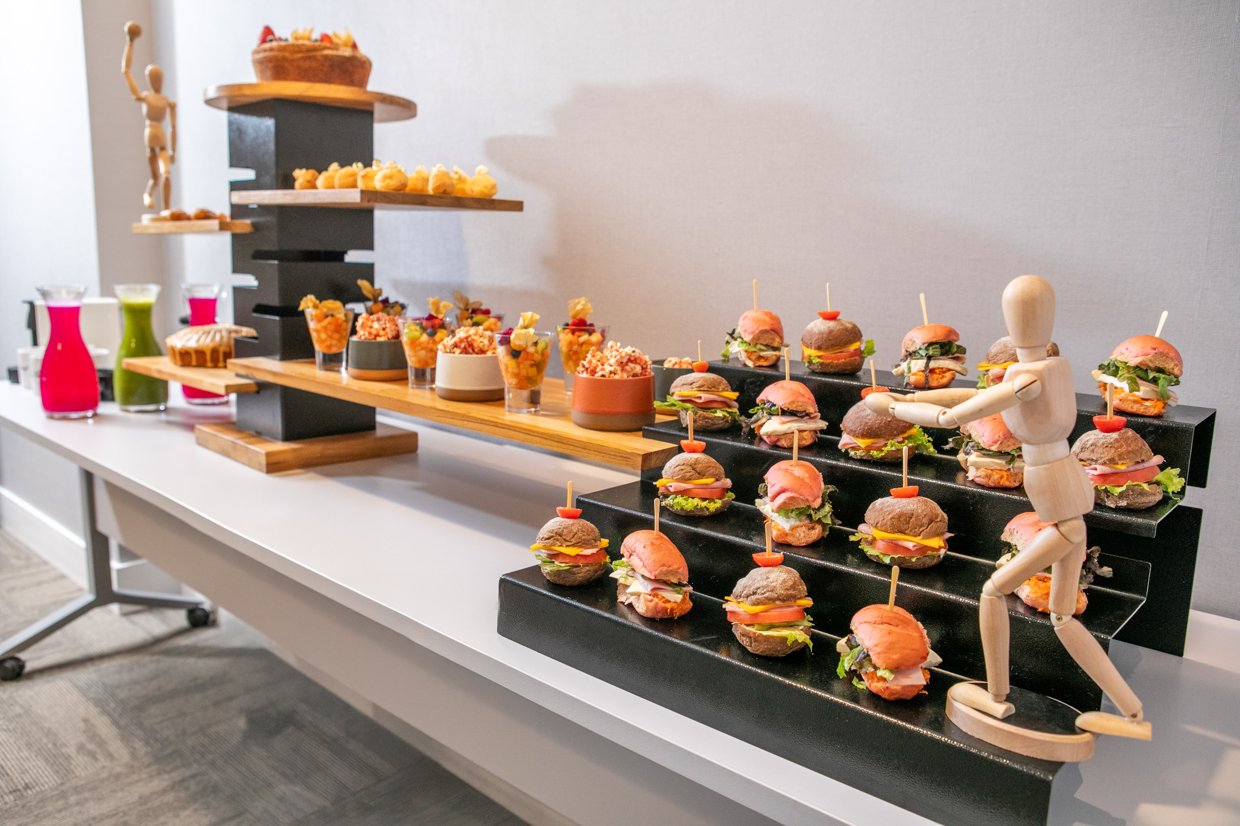 Appetizer buffet with mini burgers, fruit cups, pastries, and colorful juices.