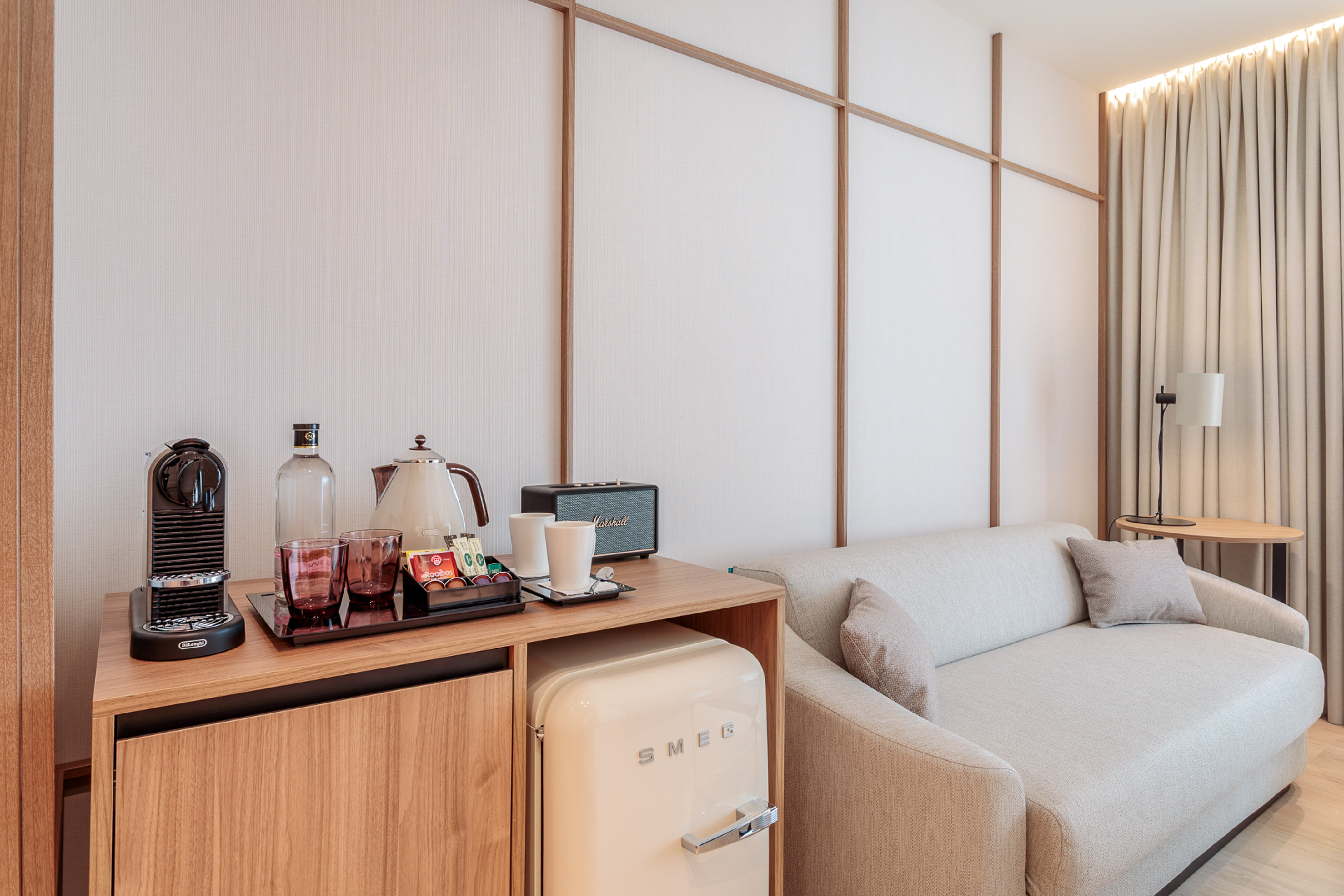Modern hotel room with coffee station, Nespresso, SMEG minibar, Marshall speaker, and sofa.