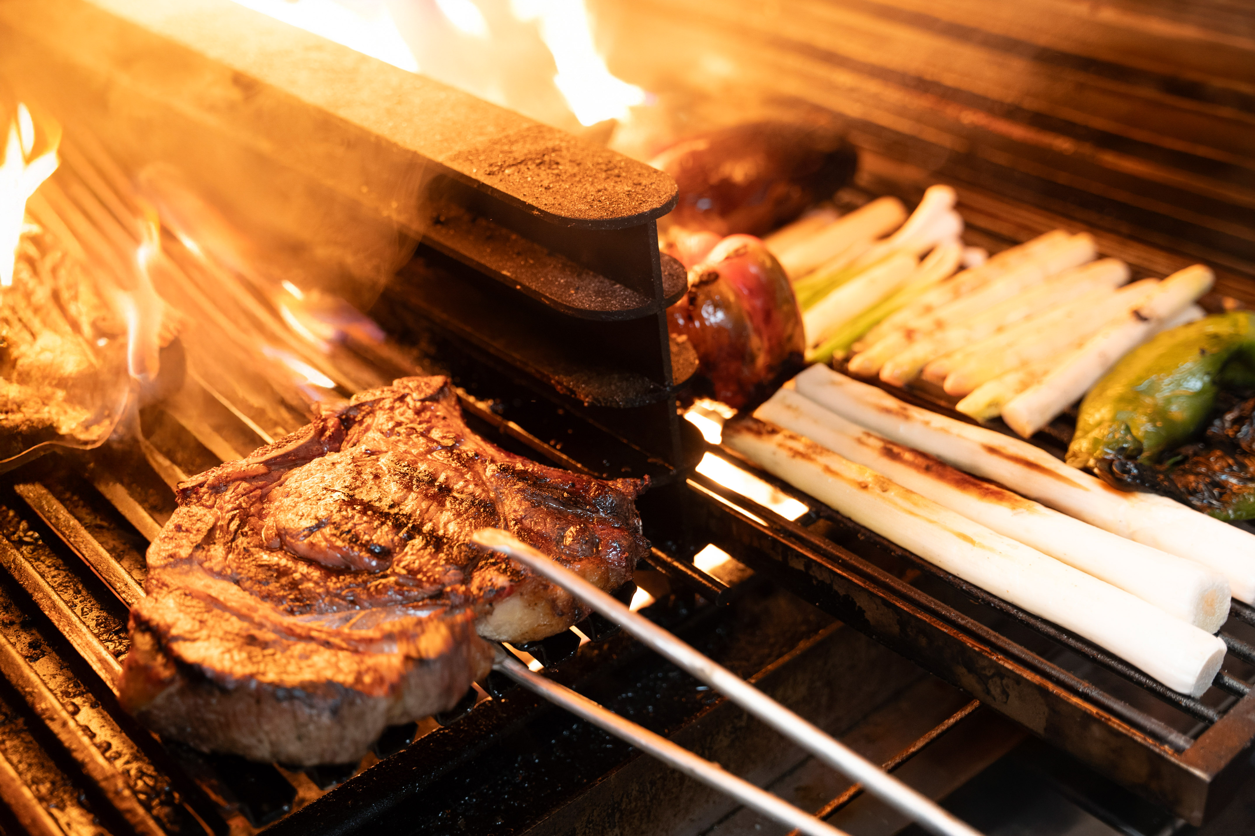 Grilling steak, leeks, and peppers over hot flames on a barbecue.