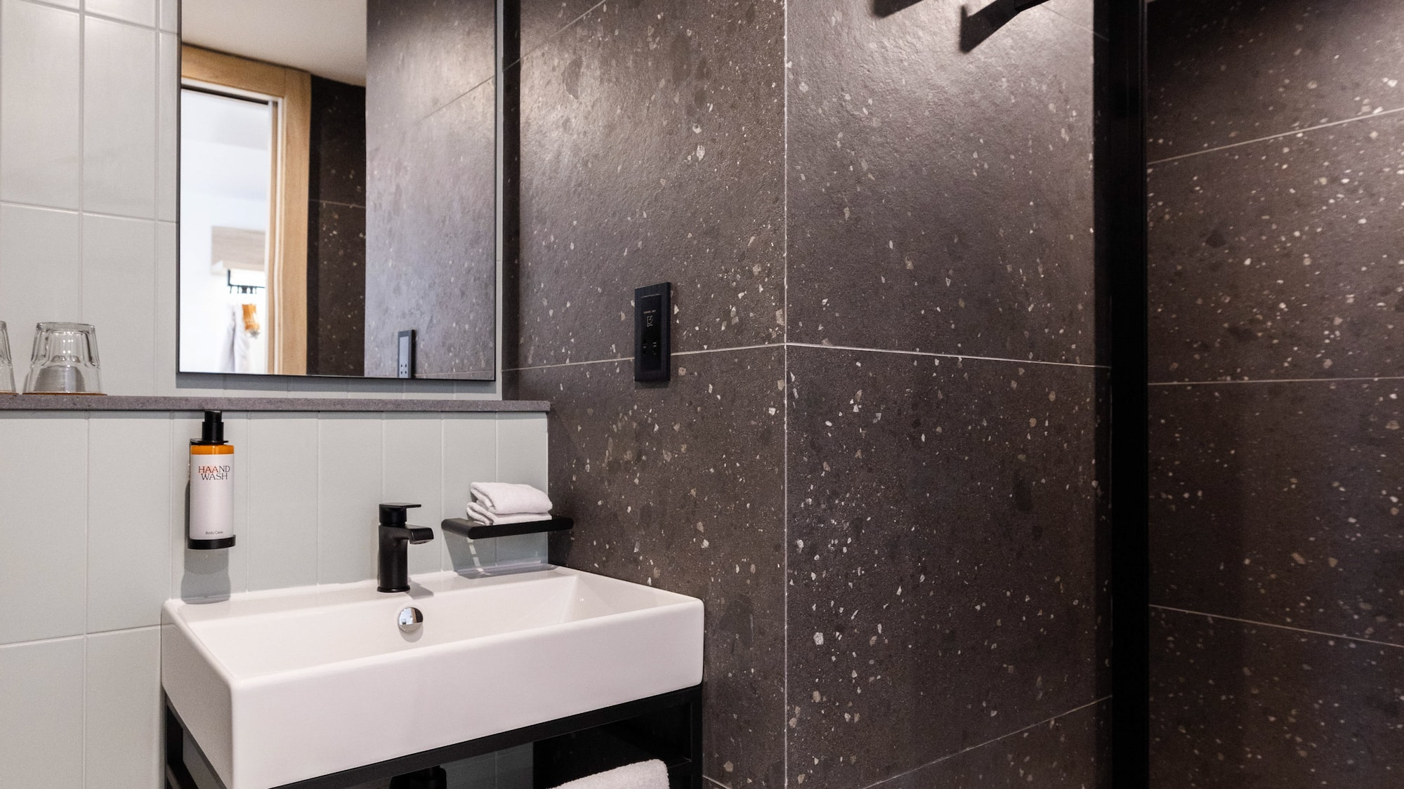 Modern bathroom with white vanity sink, dark speckled tiles, and shower.