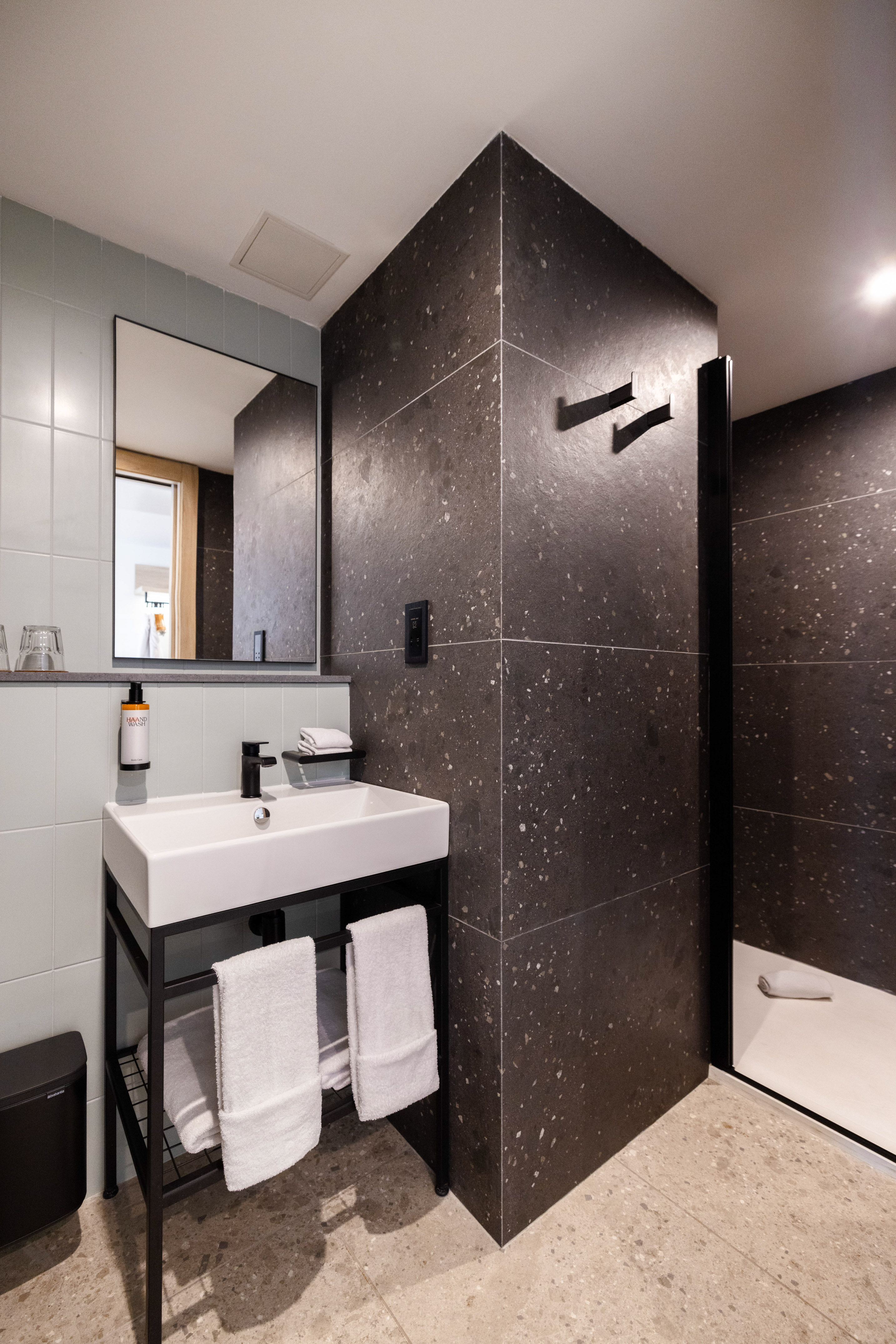 Modern bathroom with white vanity sink, dark speckled tiles, and shower.