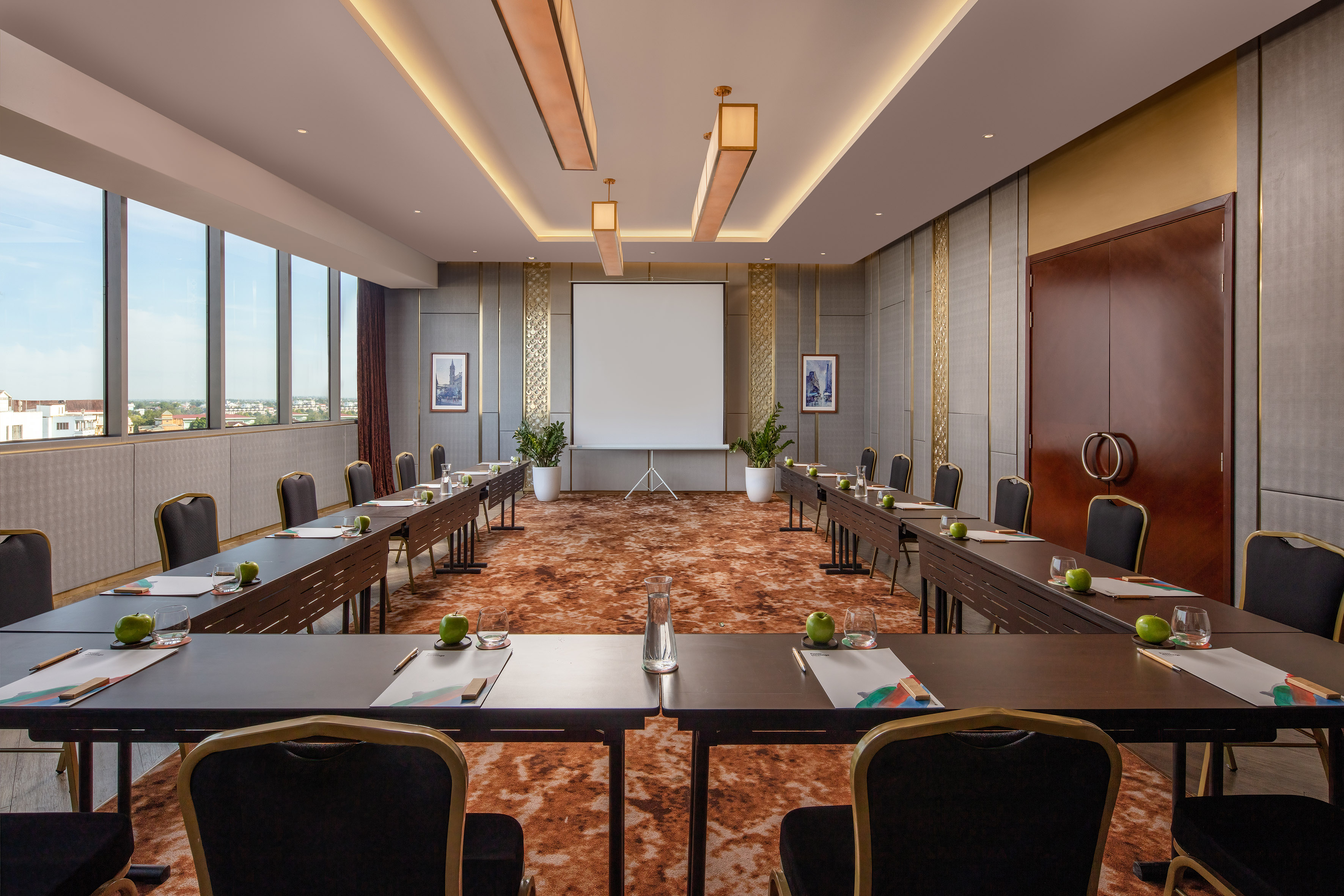 Spacious hotel meeting room with U-shaped table, projector, and city view.