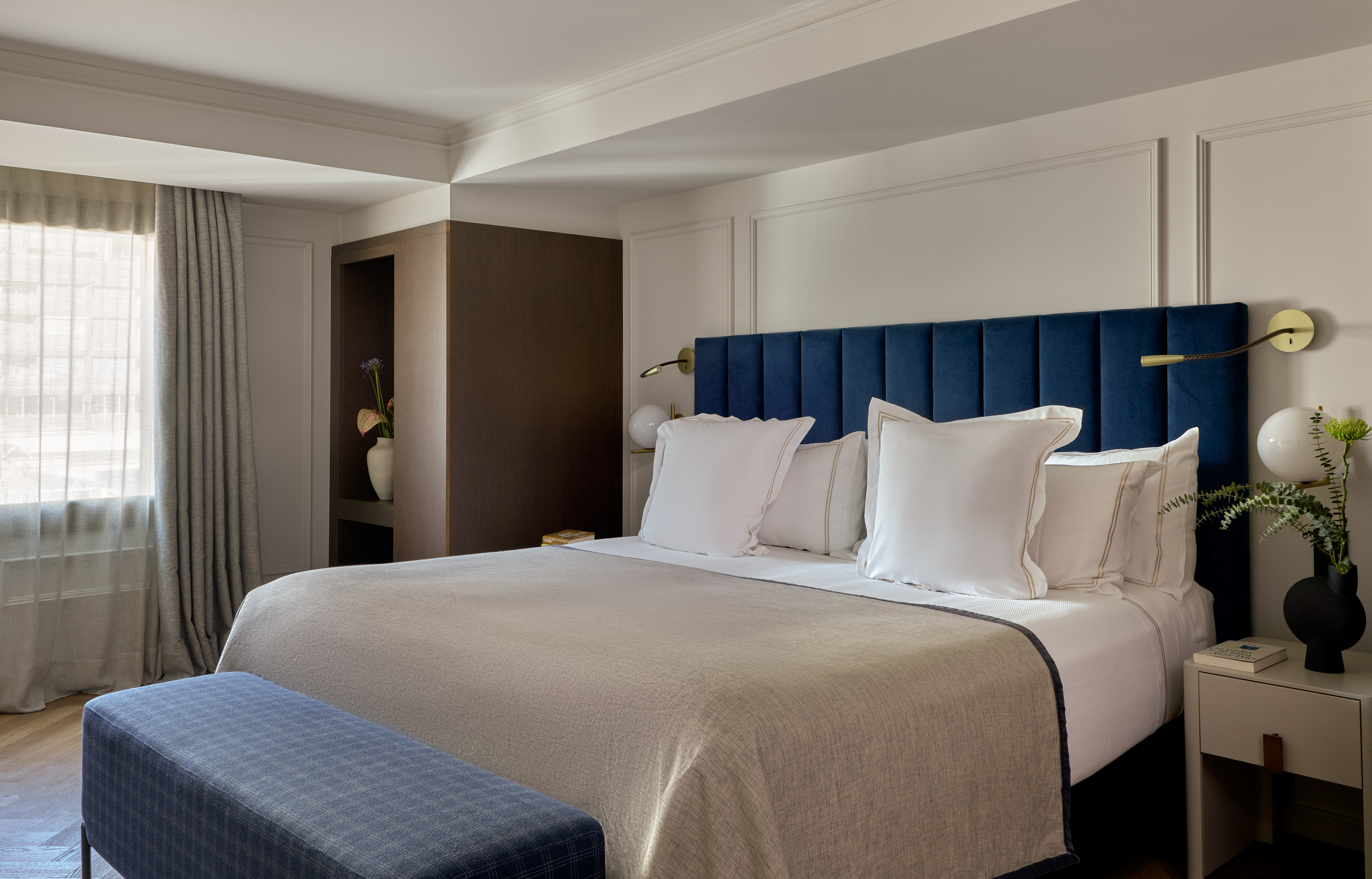 Elegant hotel bedroom with blue headboard, white bedding, and modern design.