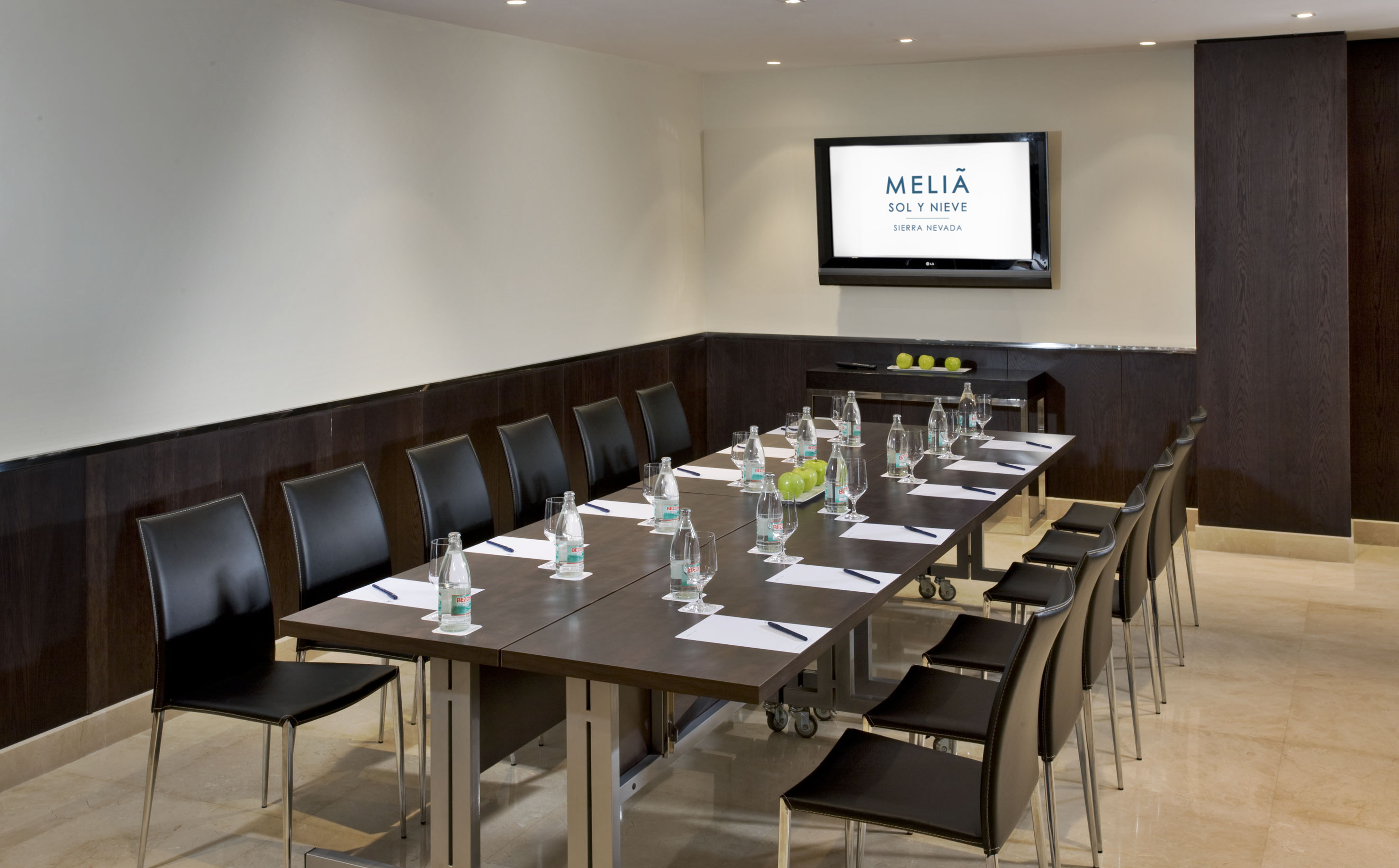 Melia conference room with long table, black chairs, water bottles, and TV.