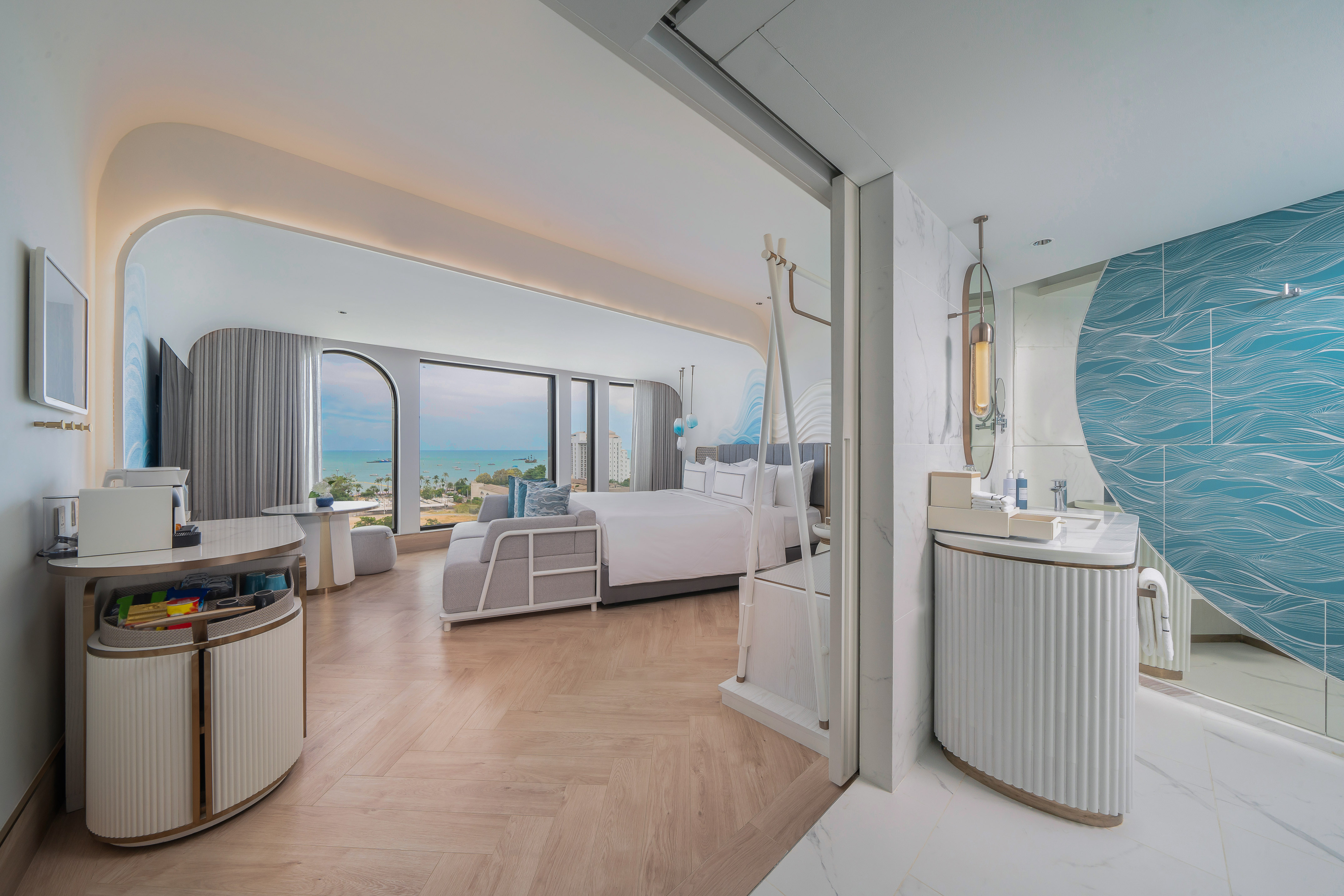 Modern hotel suite with ocean view, bedroom, and stylish blue bathroom.