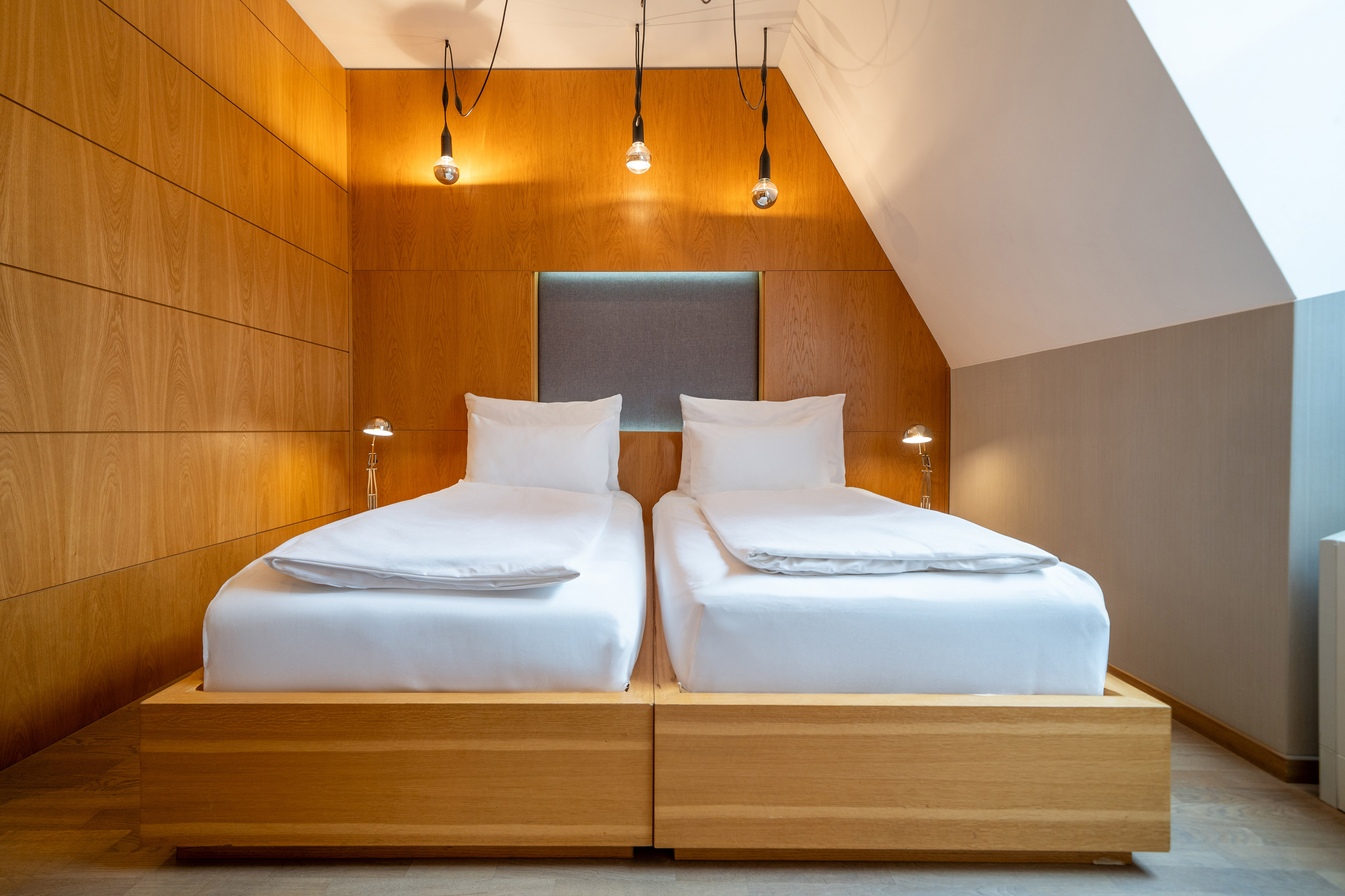 Modern twin beds in a wooden paneled bedroom with minimalist lighting.