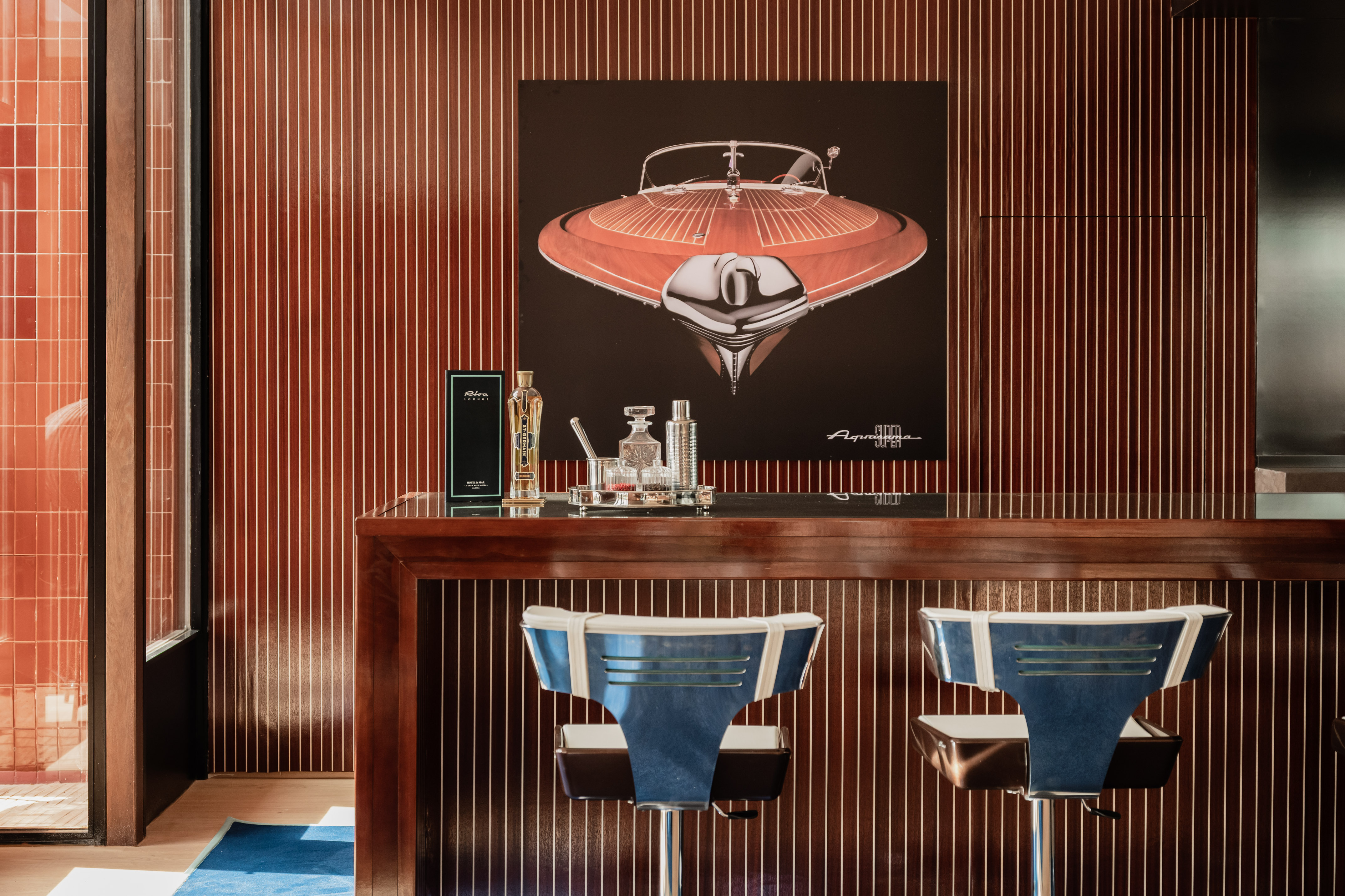 Retro bar with Aquarama boat poster, wood paneling, blue stools, and spirits.
