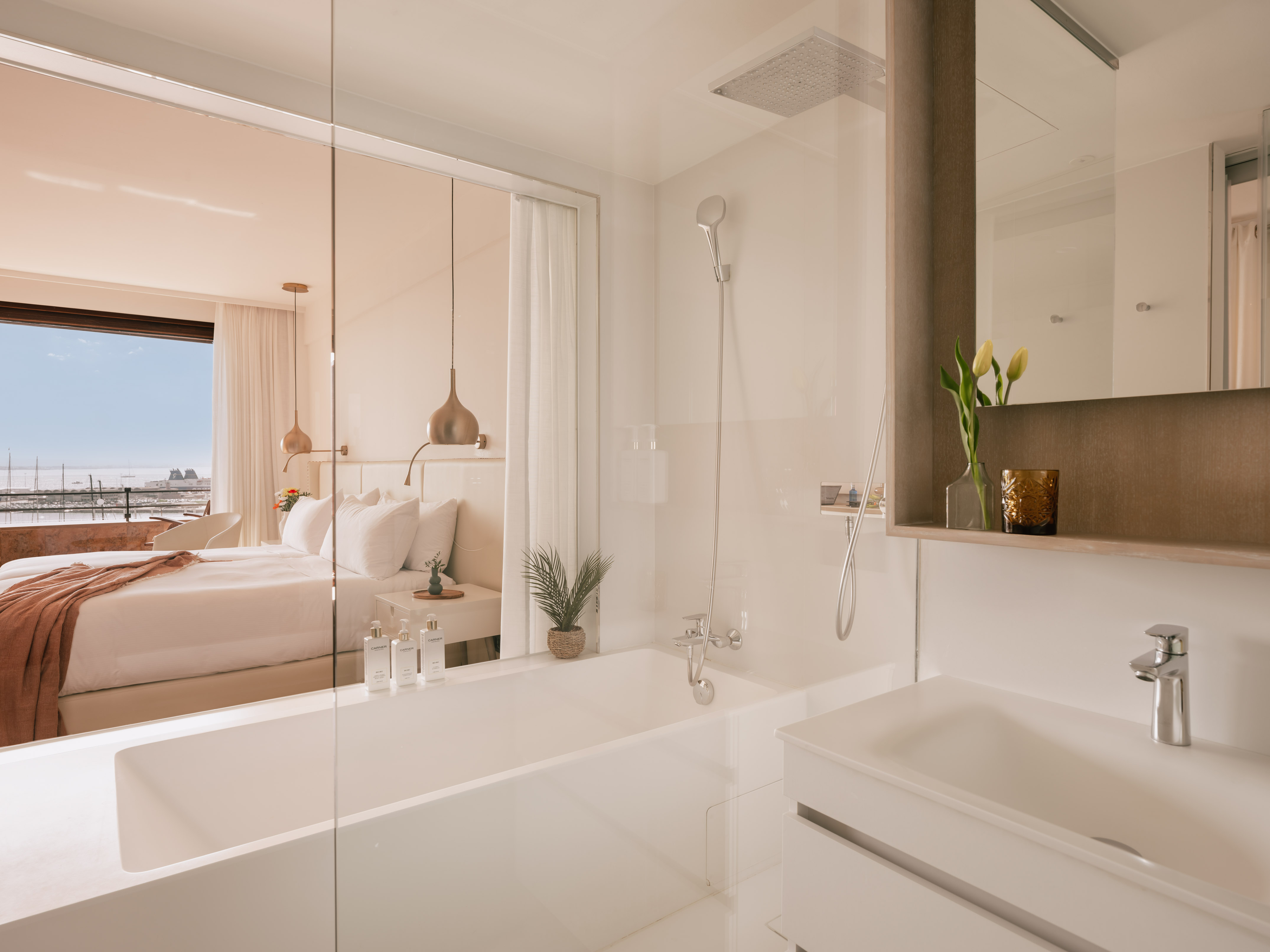 Modern hotel bathroom with bathtub, shower, and bedroom view of a harbor.