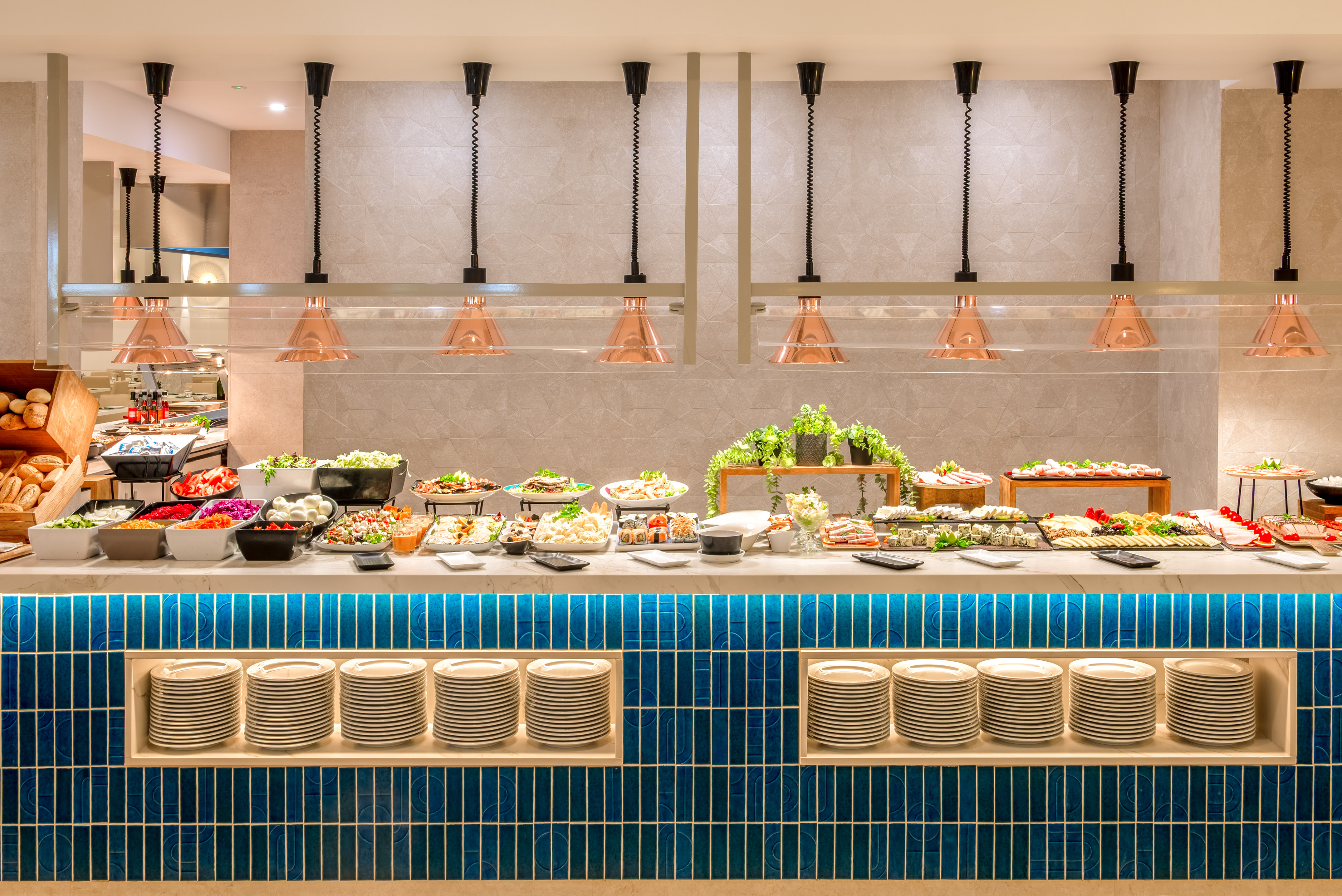 Diverse buffet with fresh salads, sushi, and bread under copper warmers.