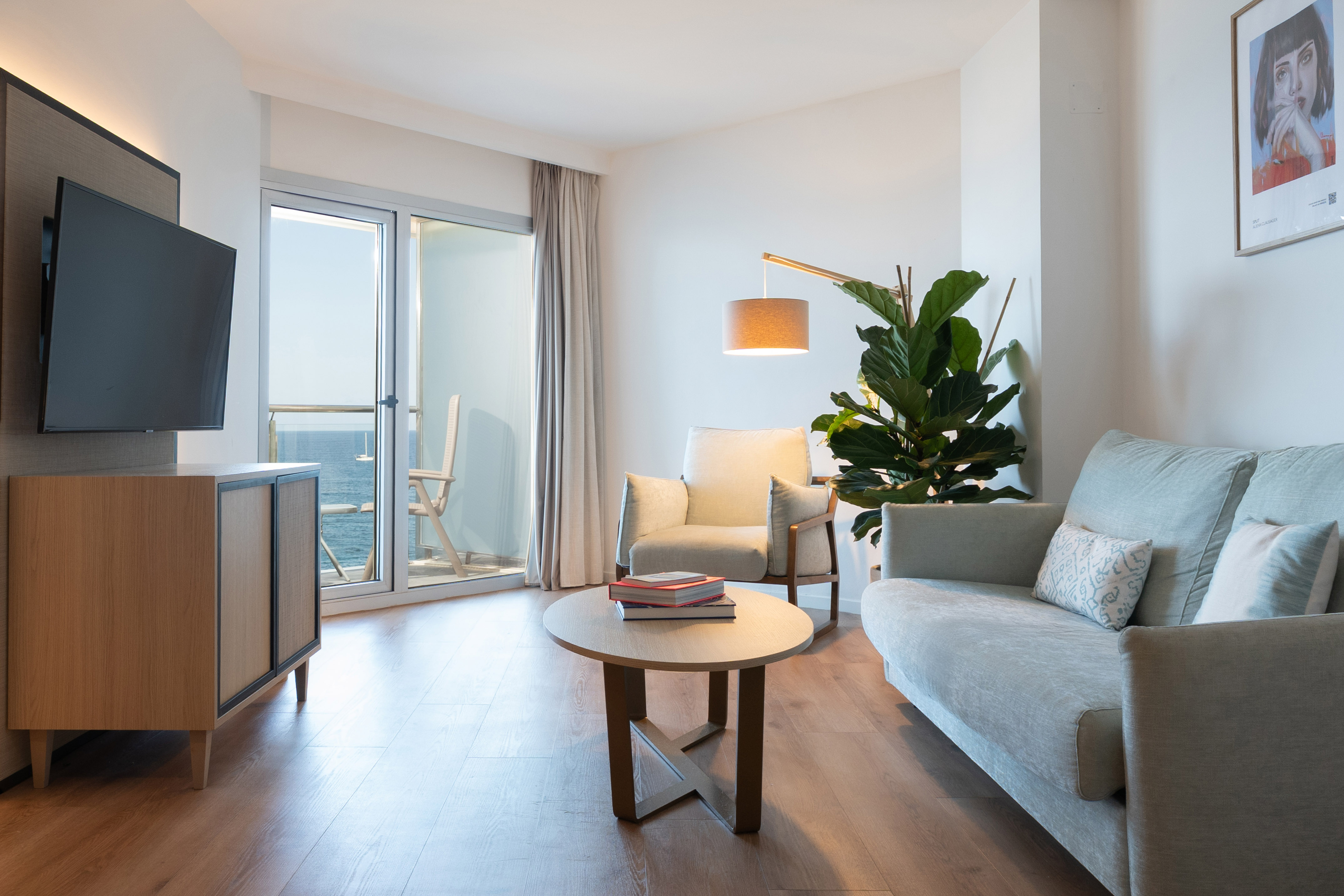 Modern hotel living room with ocean view balcony, sofa, armchair, and TV.