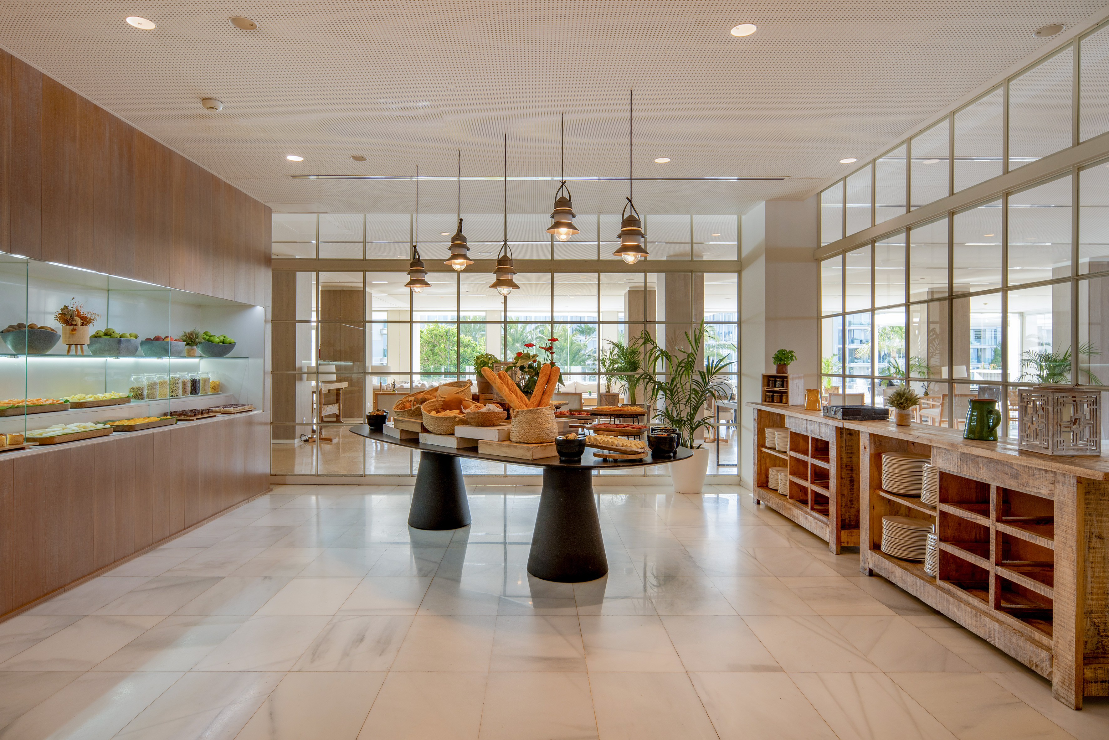 Modern hotel buffet with fresh breakfast foods, marble floor, and large windows.