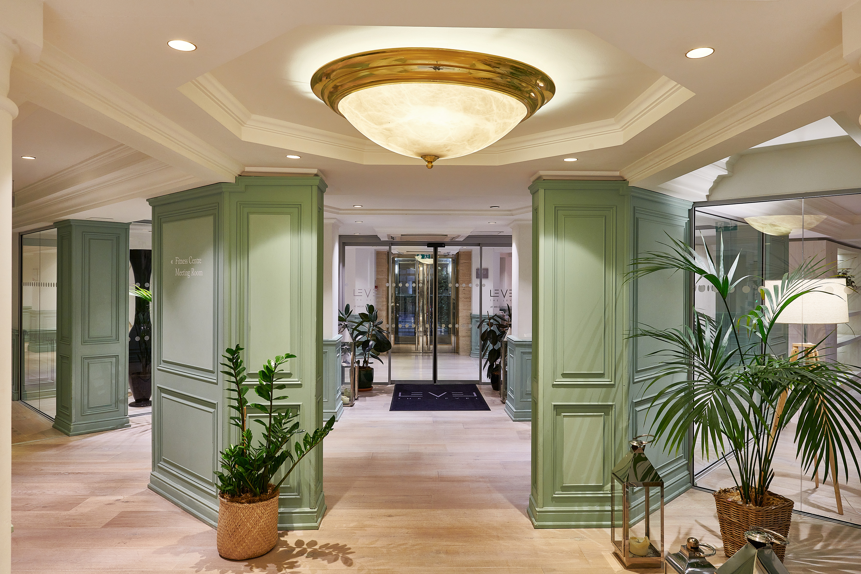 LEVEL hotel hallway featuring green paneling, wood floor, and brass ceiling light.