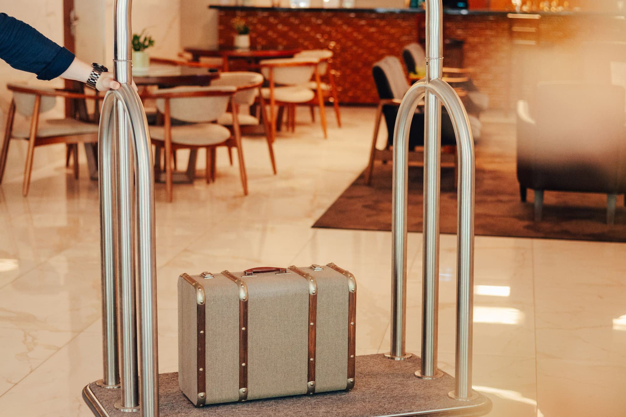Hotel luggage cart with vintage suitcase pushed through modern lobby.