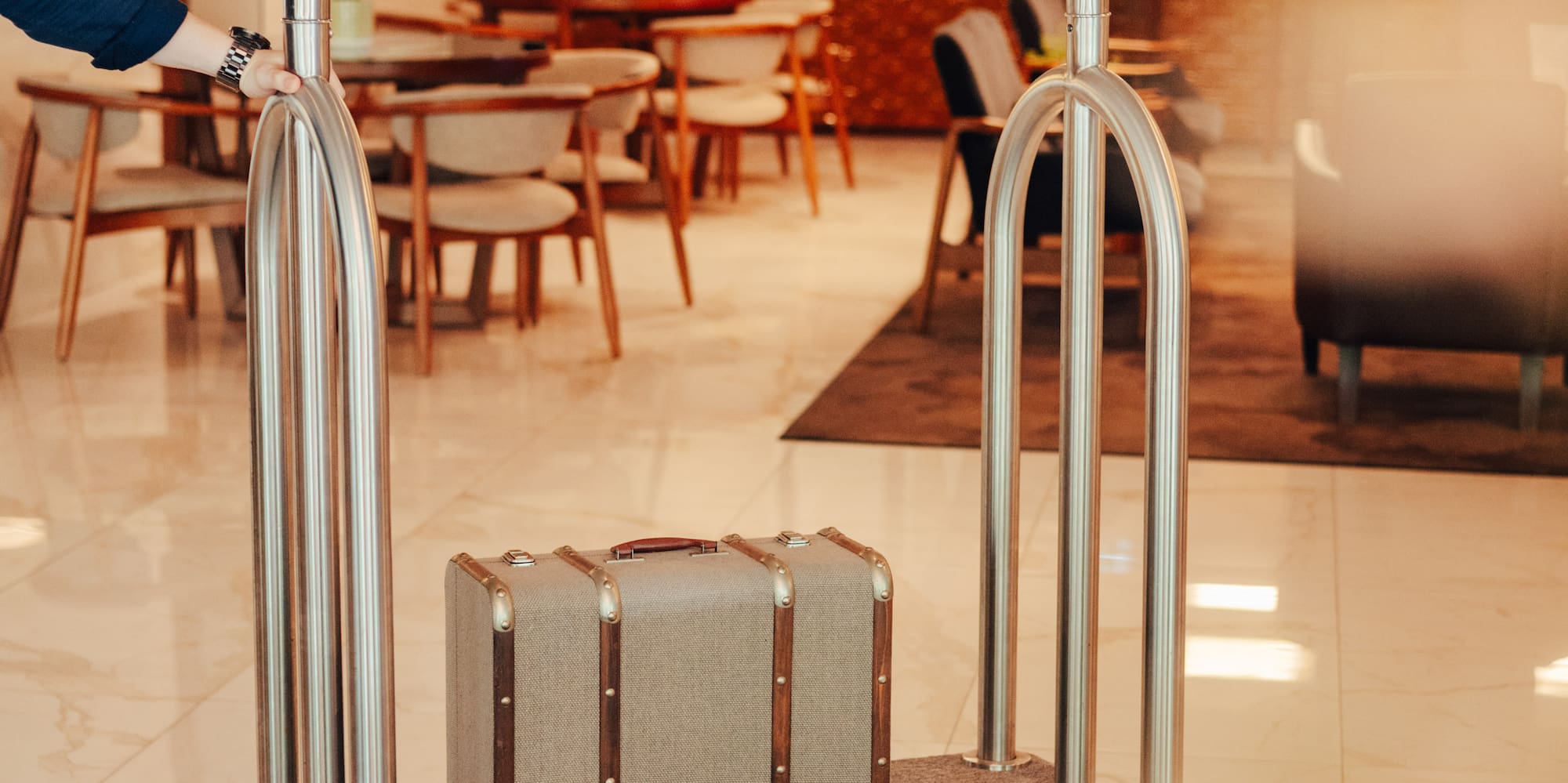 Hotel luggage cart with vintage suitcase pushed through modern lobby.