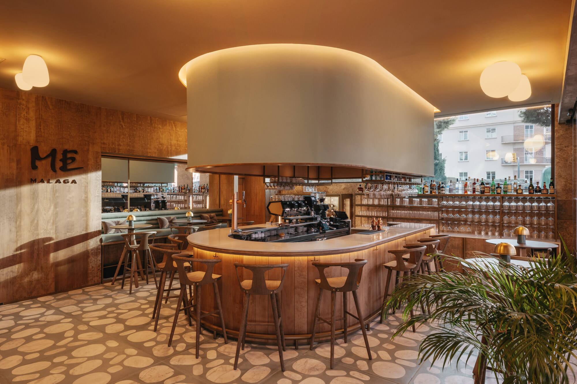ME Malaga bar: curved wooden counter, modern stools, soft ambient lighting.