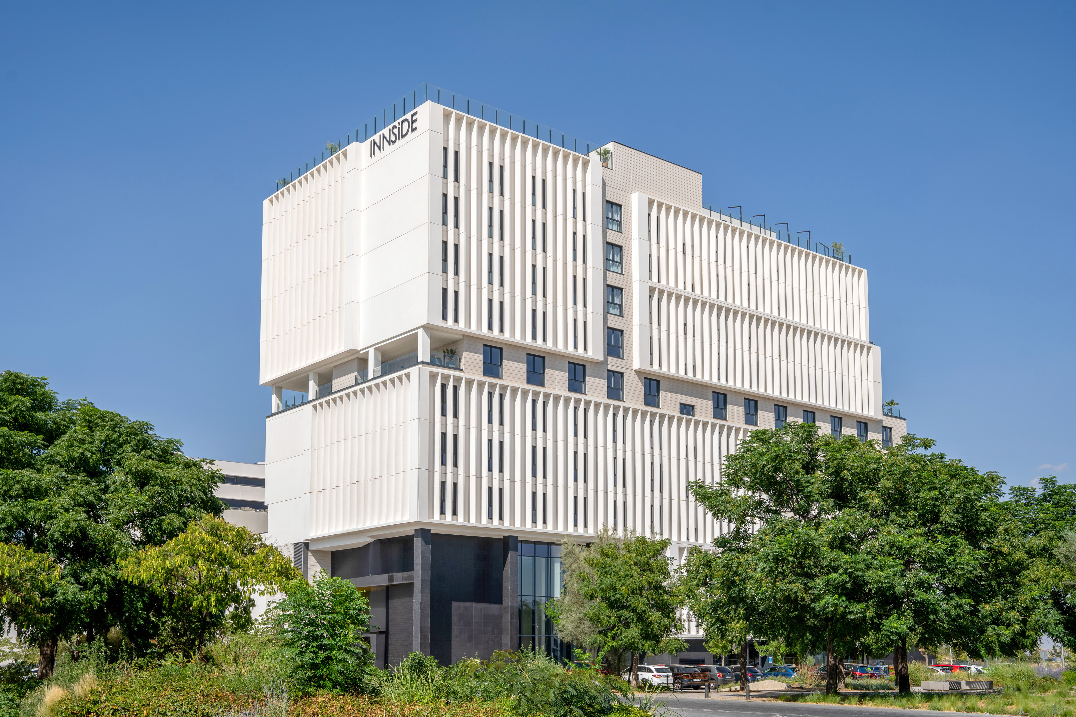 White modern Innside hotel building with vertical fins and green trees.