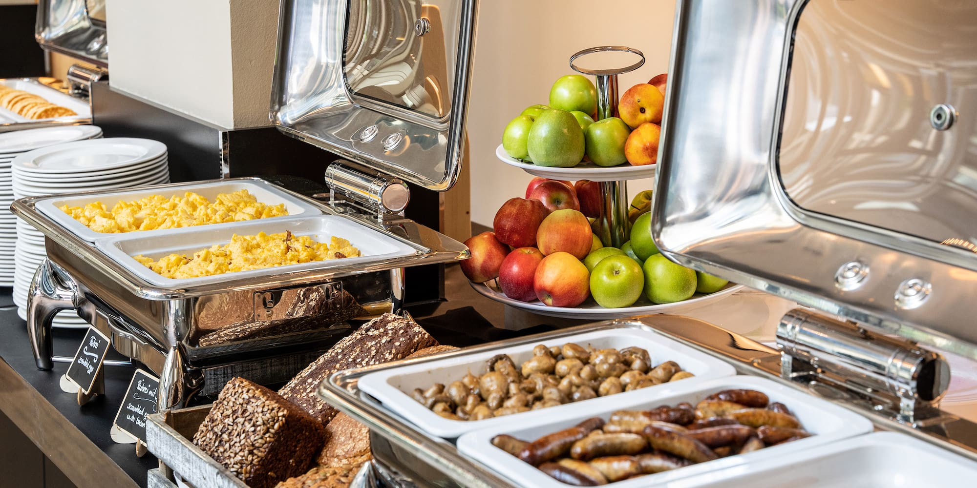 Breakfast buffet with scrambled eggs, sausages, fresh fruit, and artisan bread.