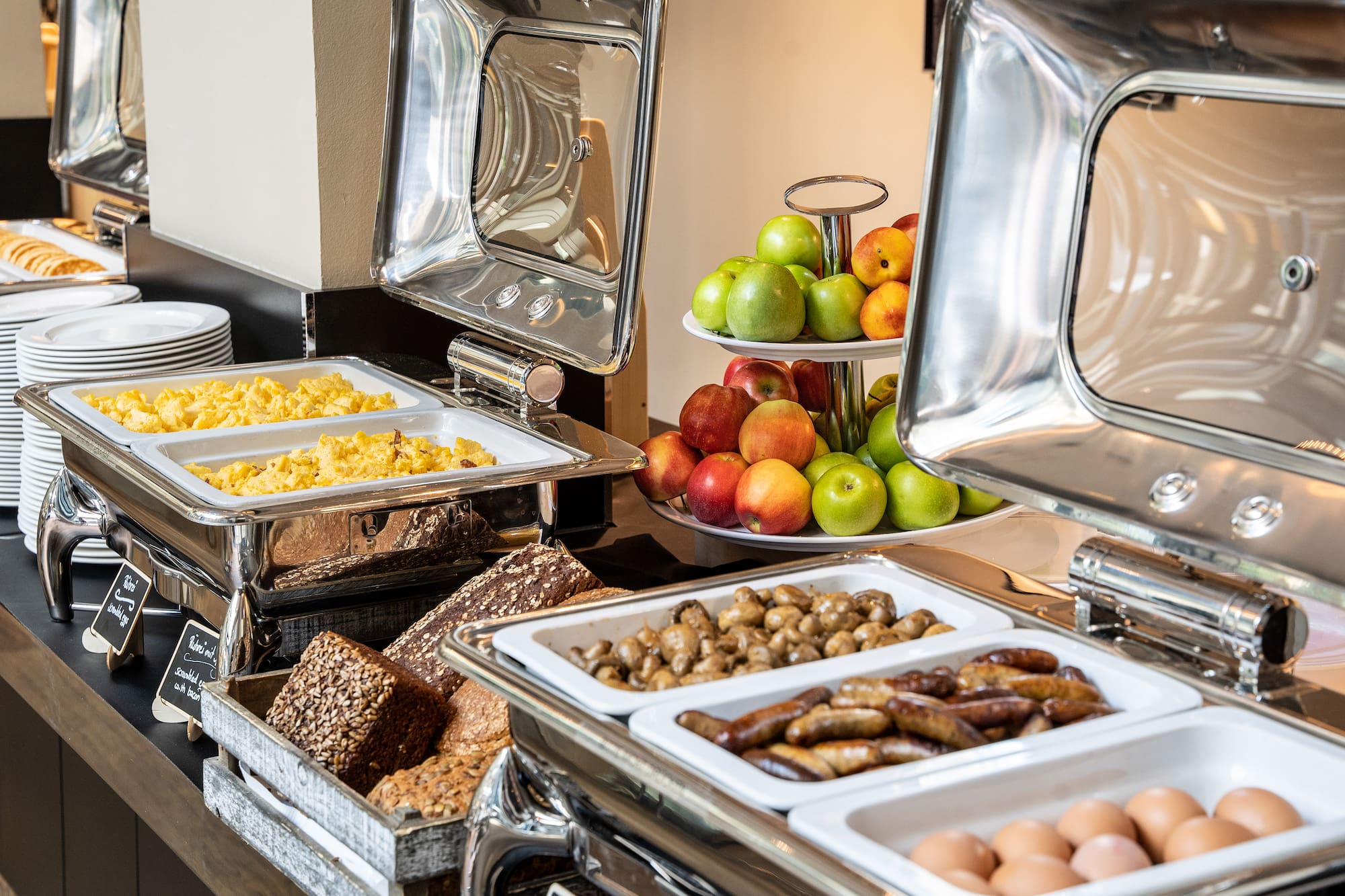 Hotel breakfast buffet with scrambled eggs, sausages, fresh fruit, and bread.