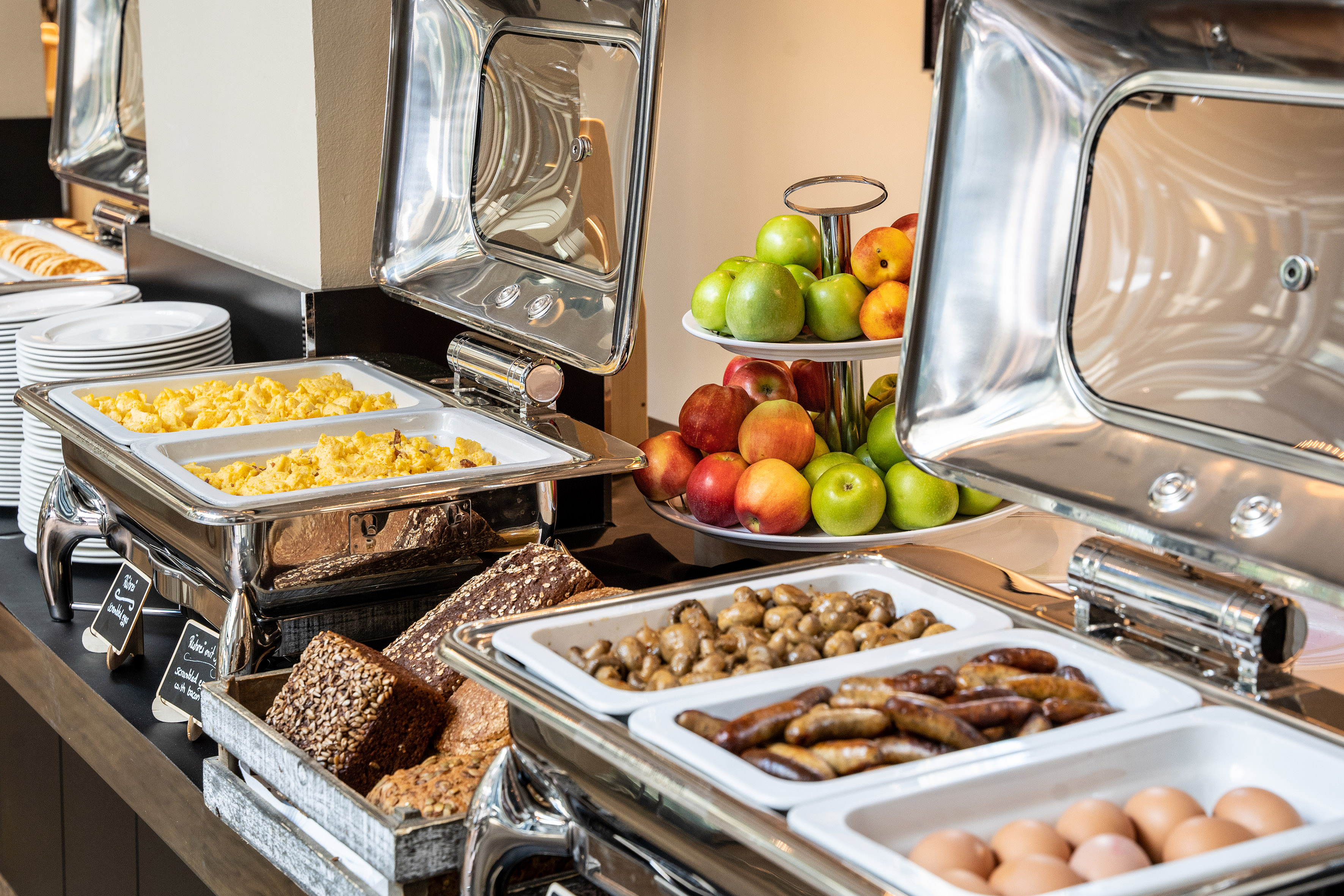 Breakfast buffet with scrambled eggs, sausages, fresh fruit, and artisan bread.