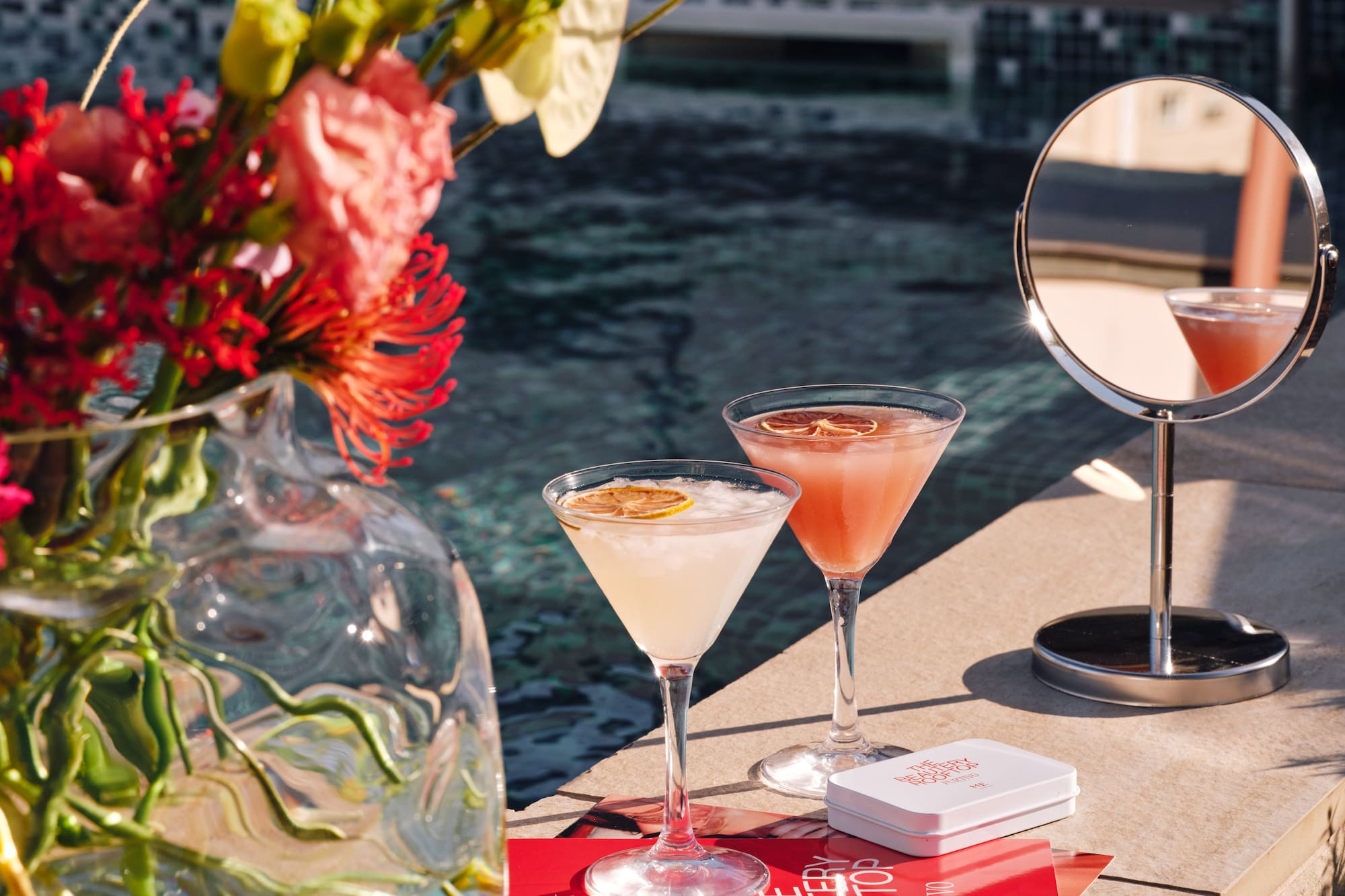 Rooftop pool cocktails with flowers, mirror, and Beauty Rooftop menu.