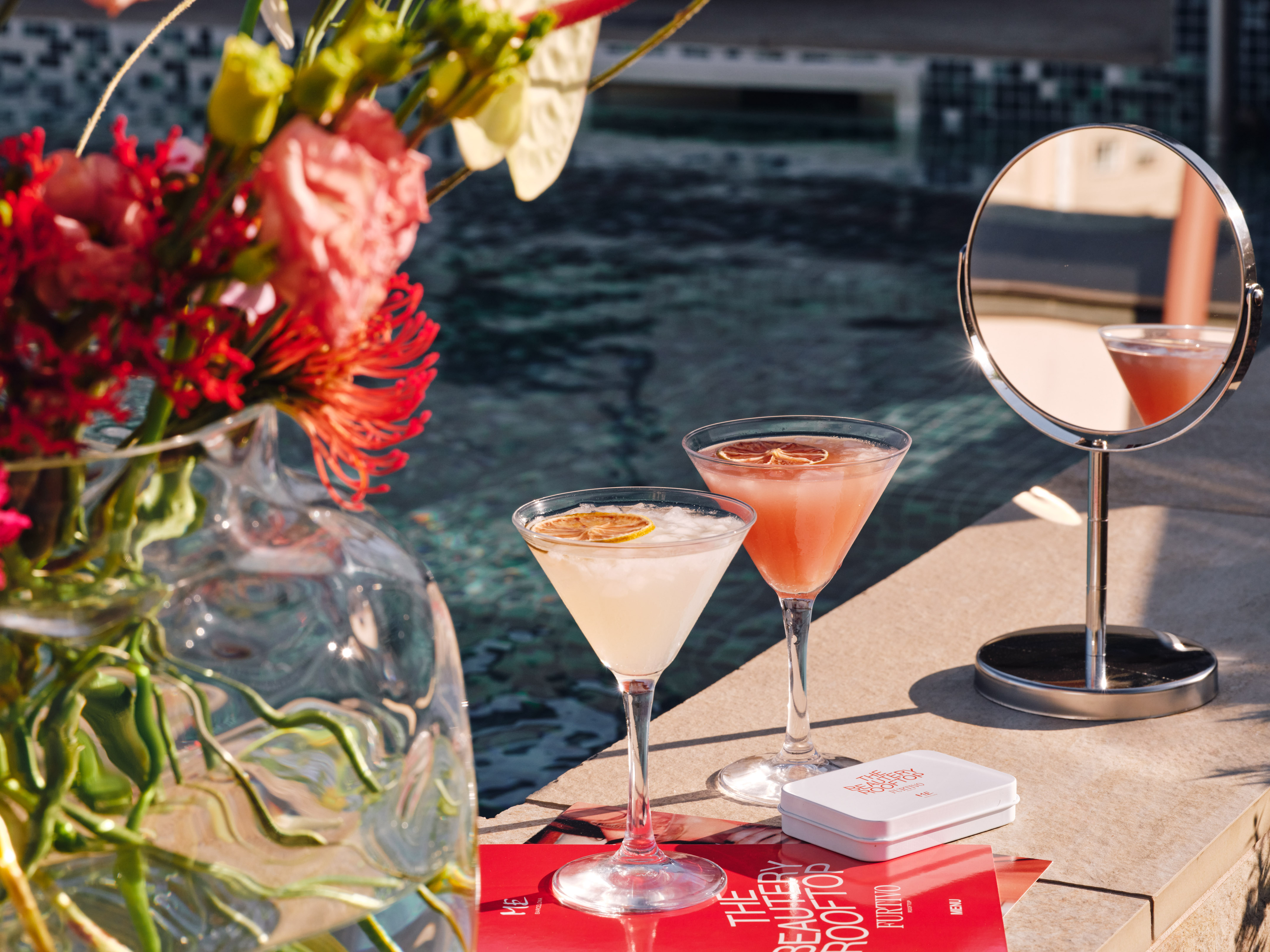 Rooftop pool cocktails with flowers, mirror, and Beauty Rooftop menu.