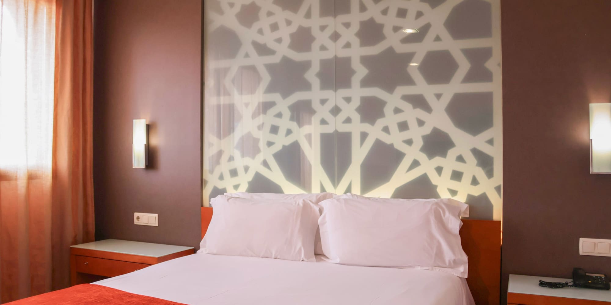 a bed with white pillows and a wall with a light on it