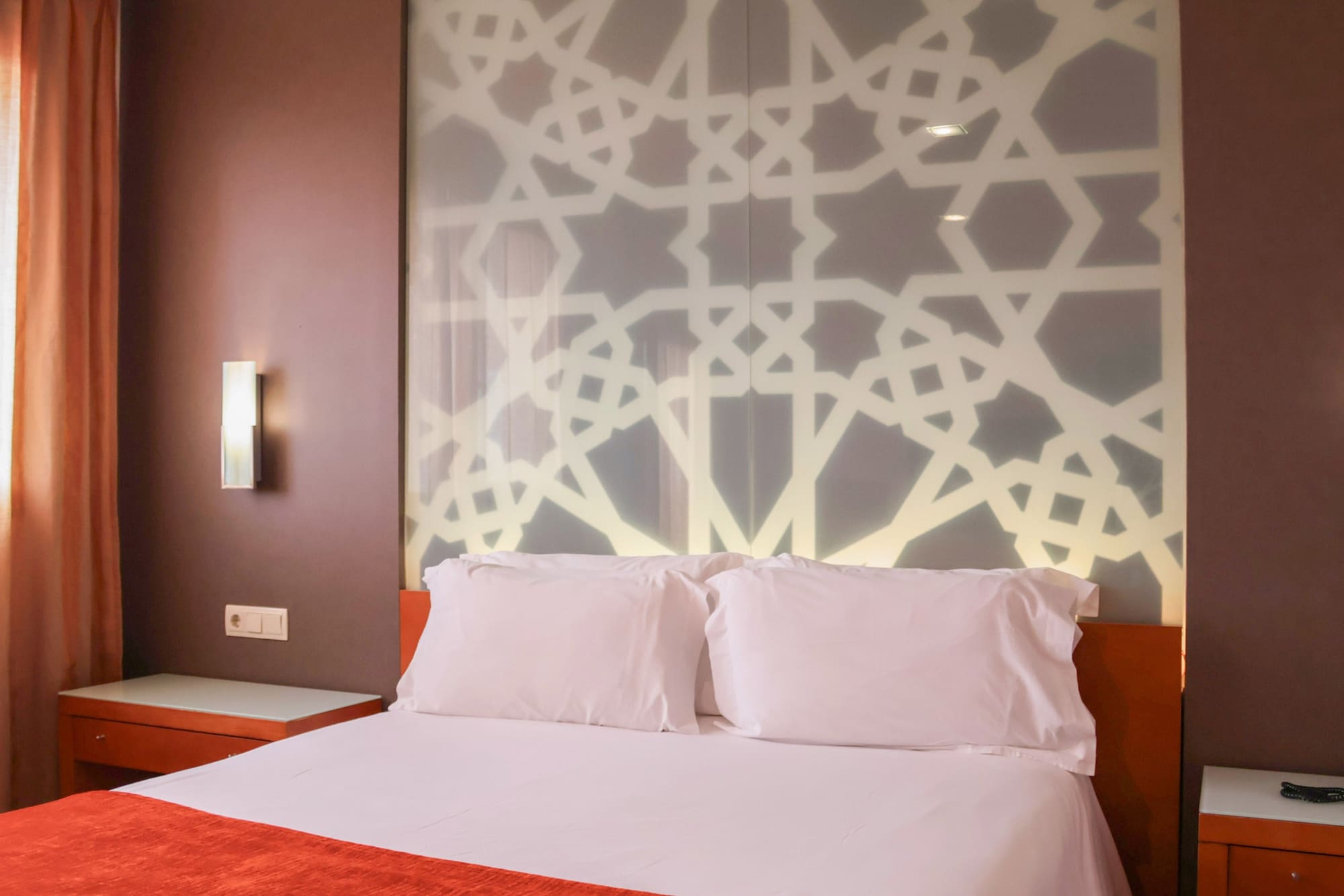 a bed with white pillows and a wall with a light on it