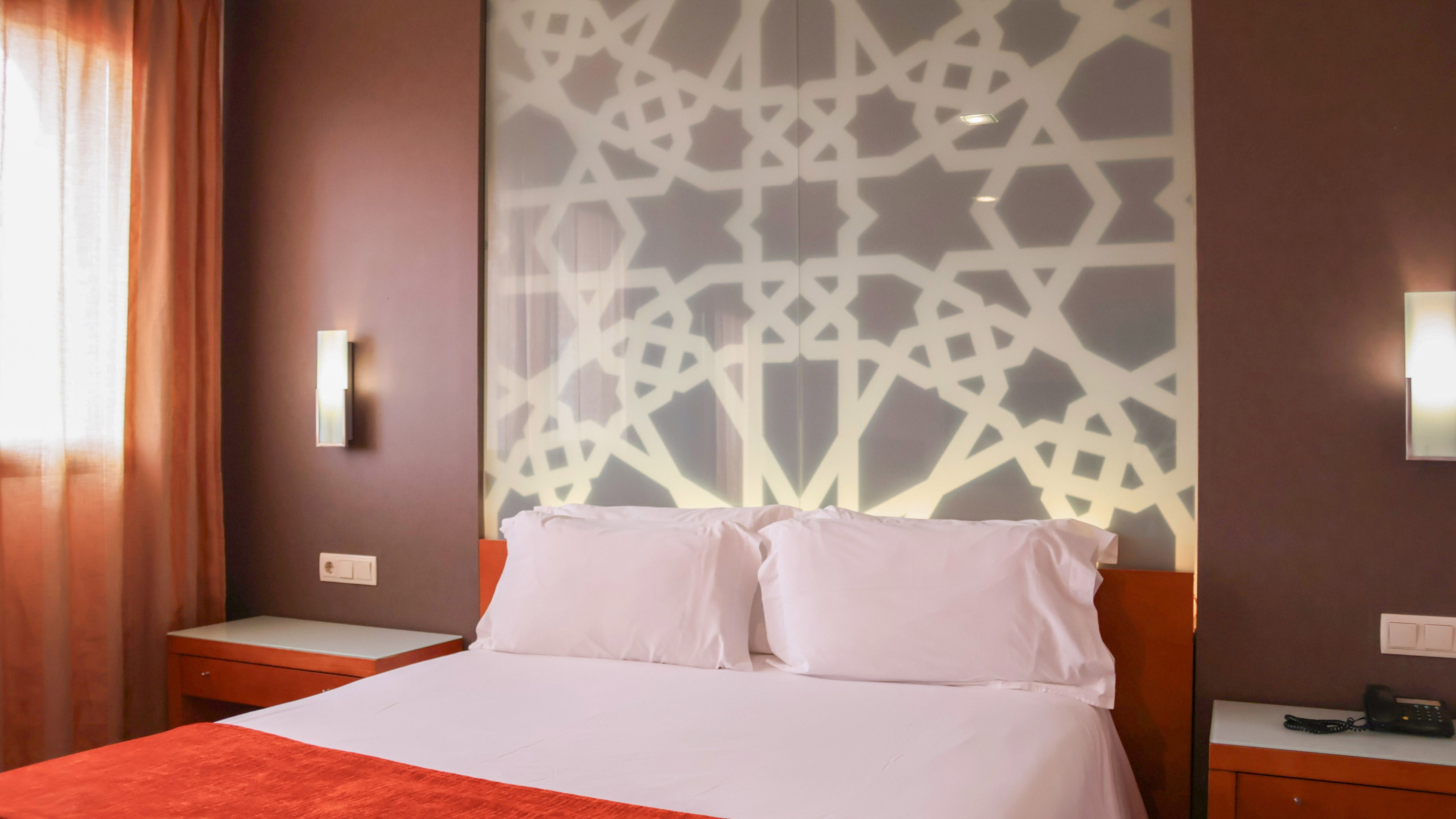 Modern hotel room with king bed, geometric headboard, and warm orange accents.