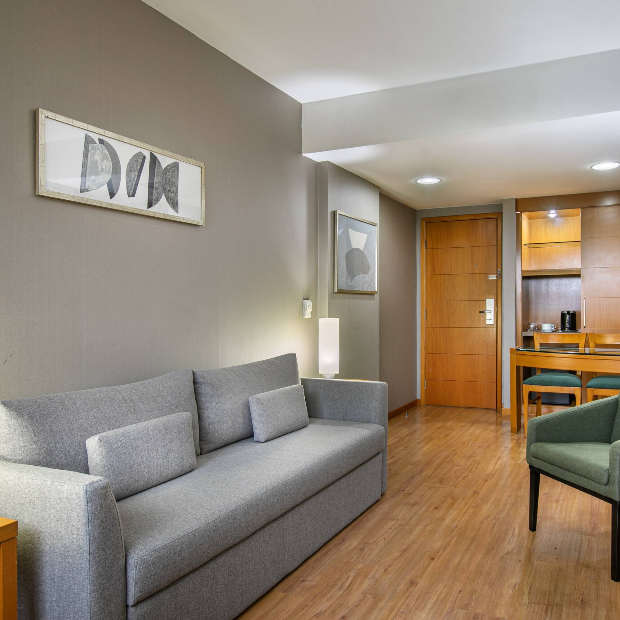Modern living area with gray sofa, green accent chair, wood floor, and dining nook.