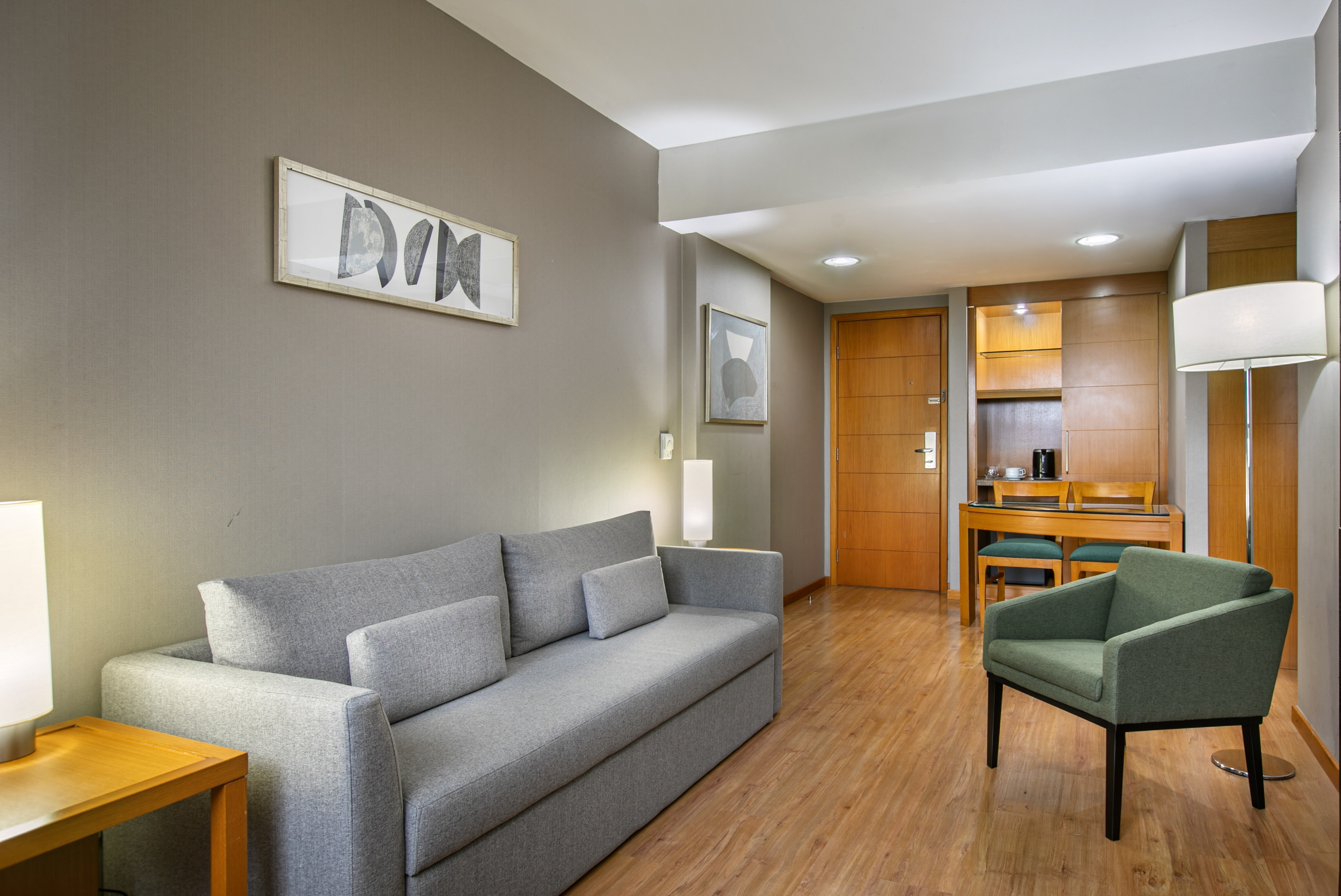 Modern living area with gray sofa, green accent chair, wood floor, and dining nook.