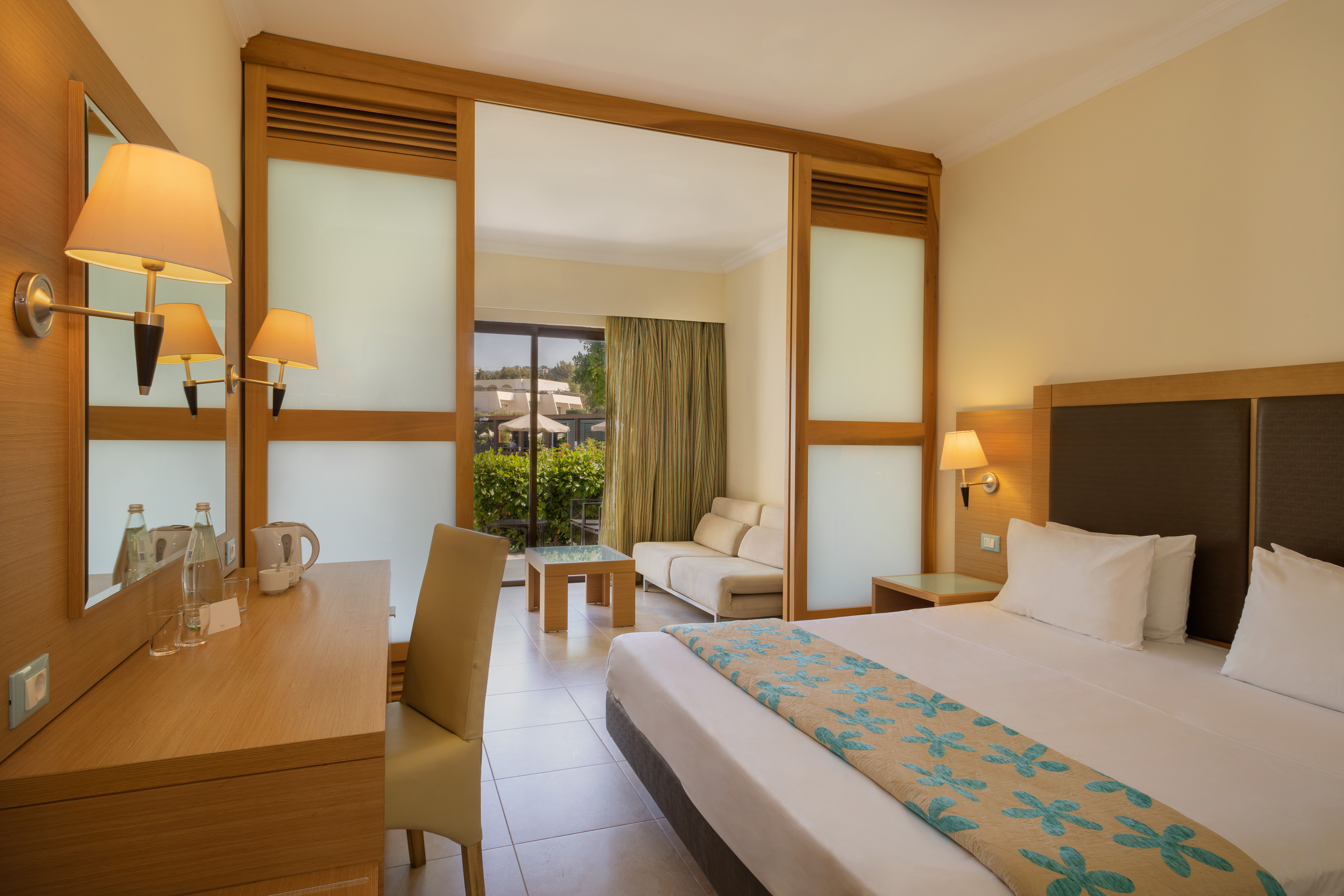 Modern hotel room with king bed, desk, sofa lounge, and balcony access.