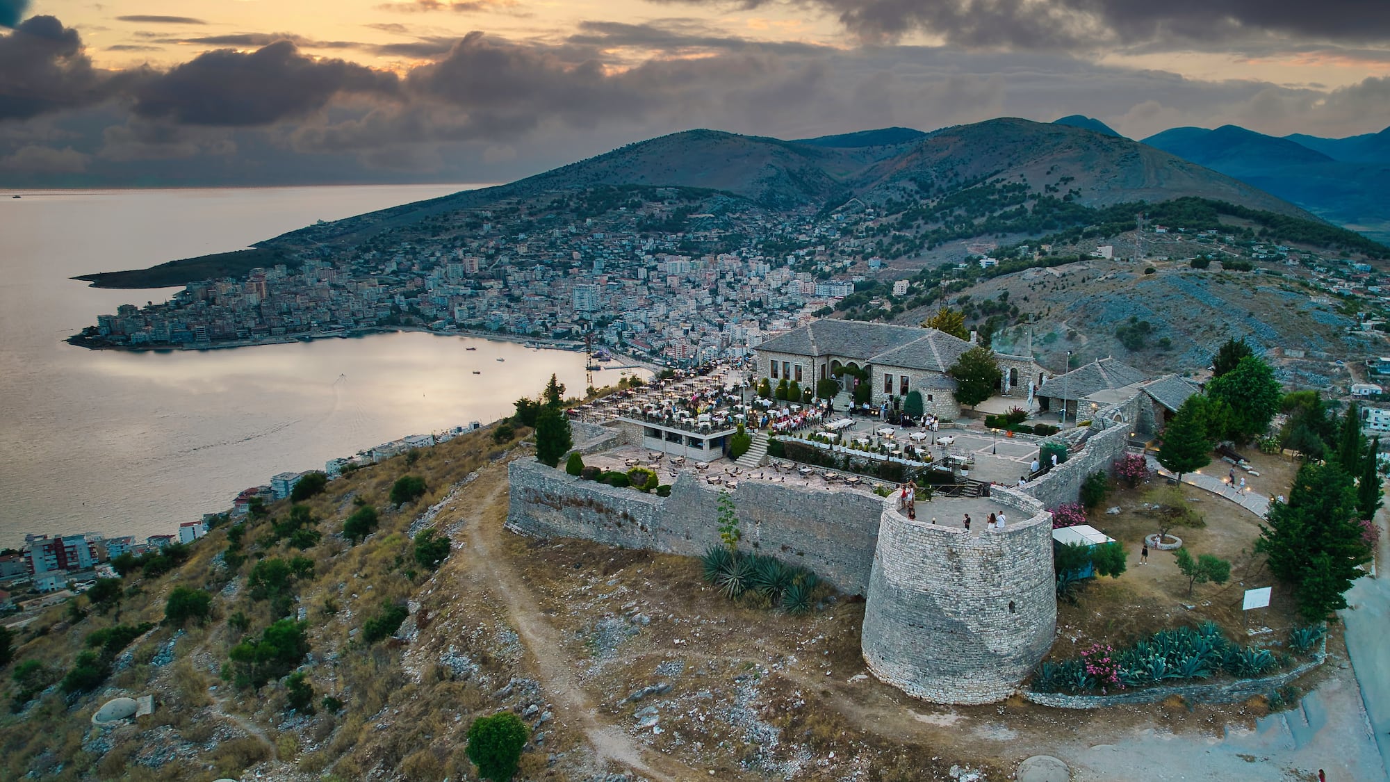 a stone building on a hill with a body of water in the background