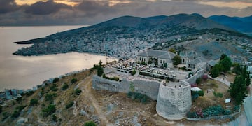 a stone building on a hill with a body of water in the background