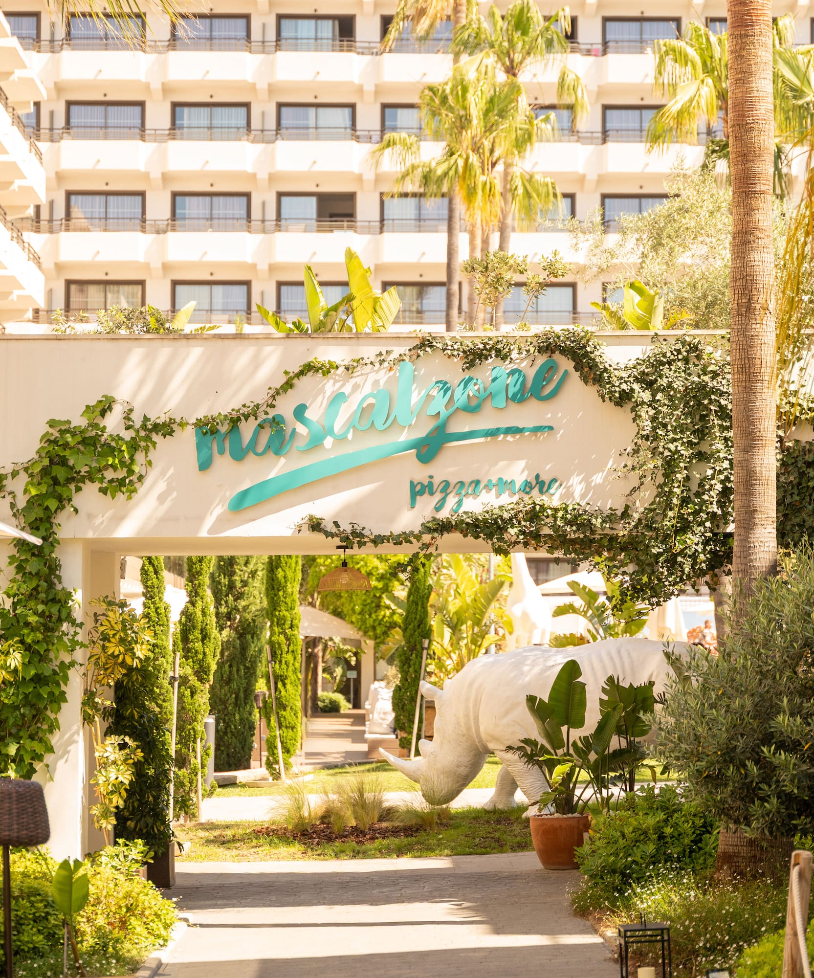 Mascalzone pizzamore entrance, tropical palms, ivy arch, white rhino statue.